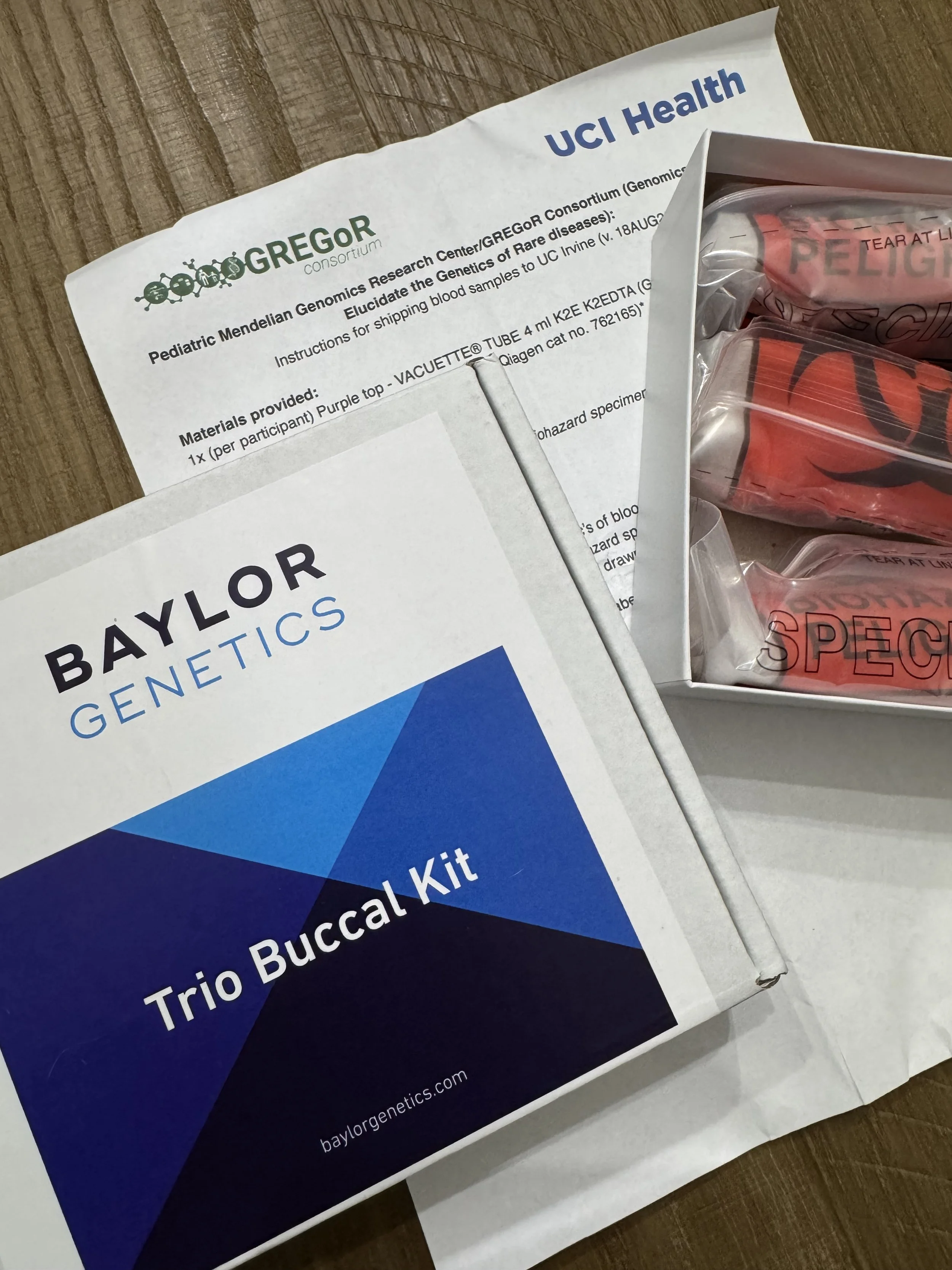Pediatric Genetics Research Kit package and blood sample vials on wooden surface.