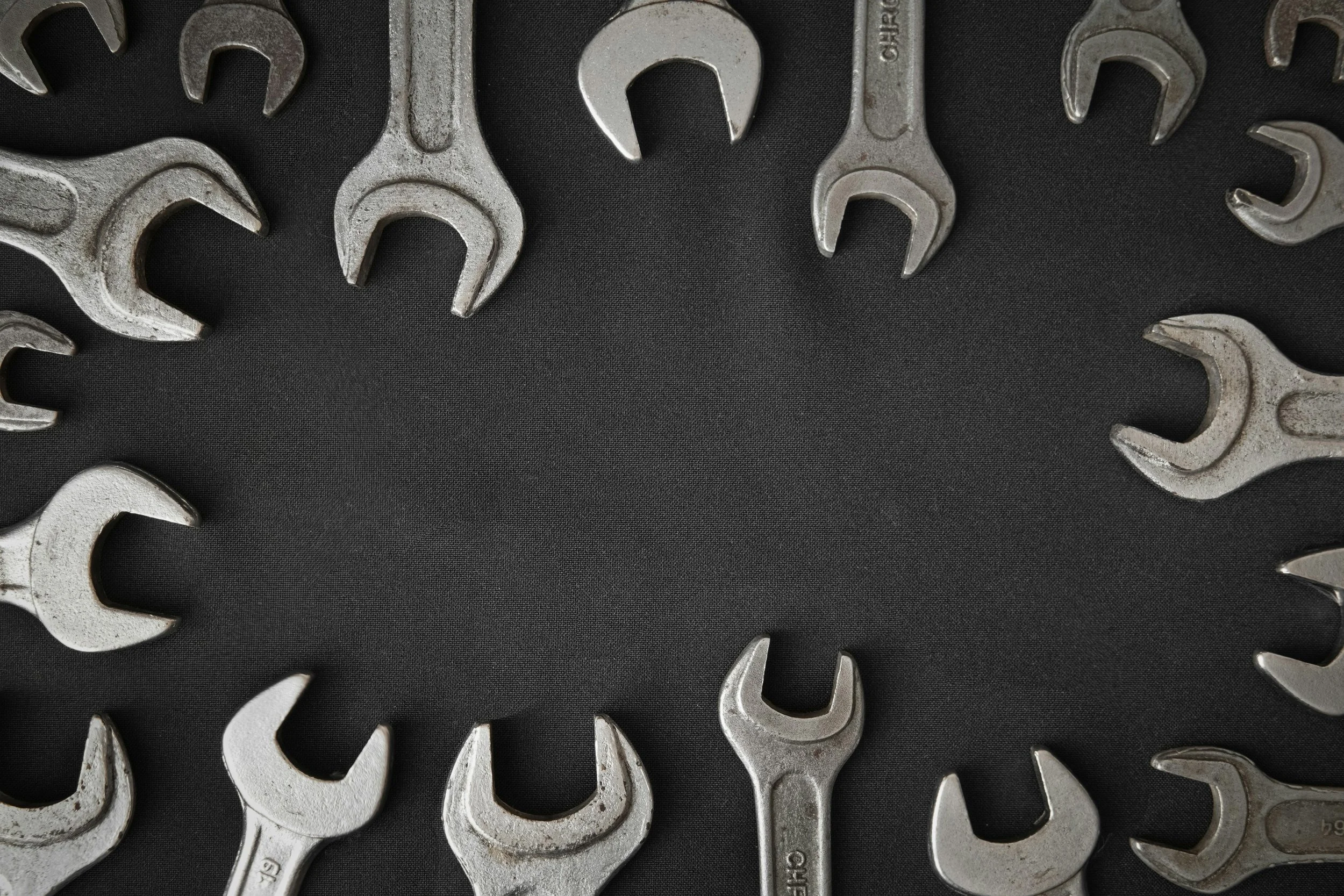 Metal wrenches arranged in a circular pattern on a black fabric background, creating a frame with space in the center.