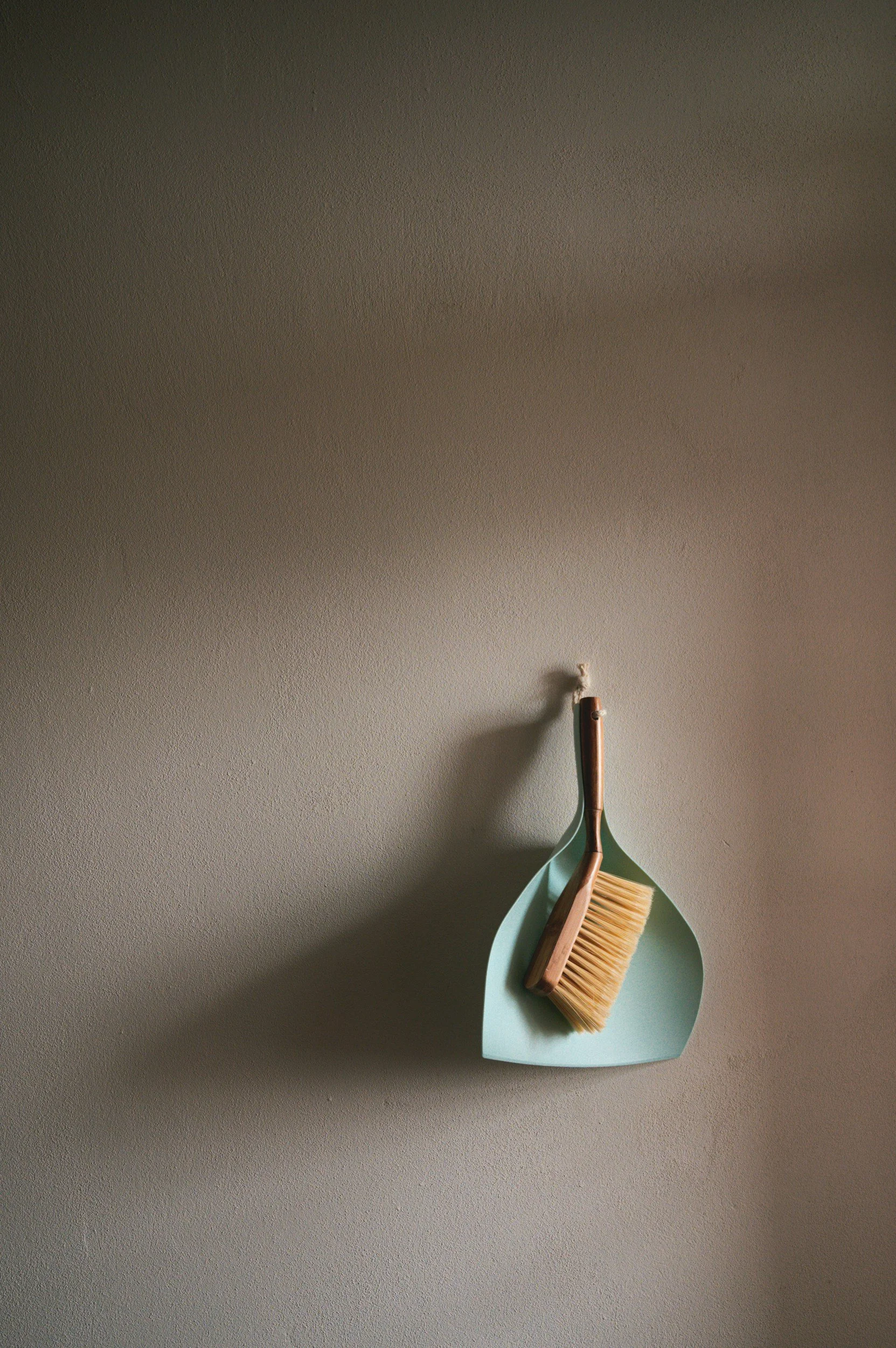 Cleaning brush and dustpan hanging on a beige wall.