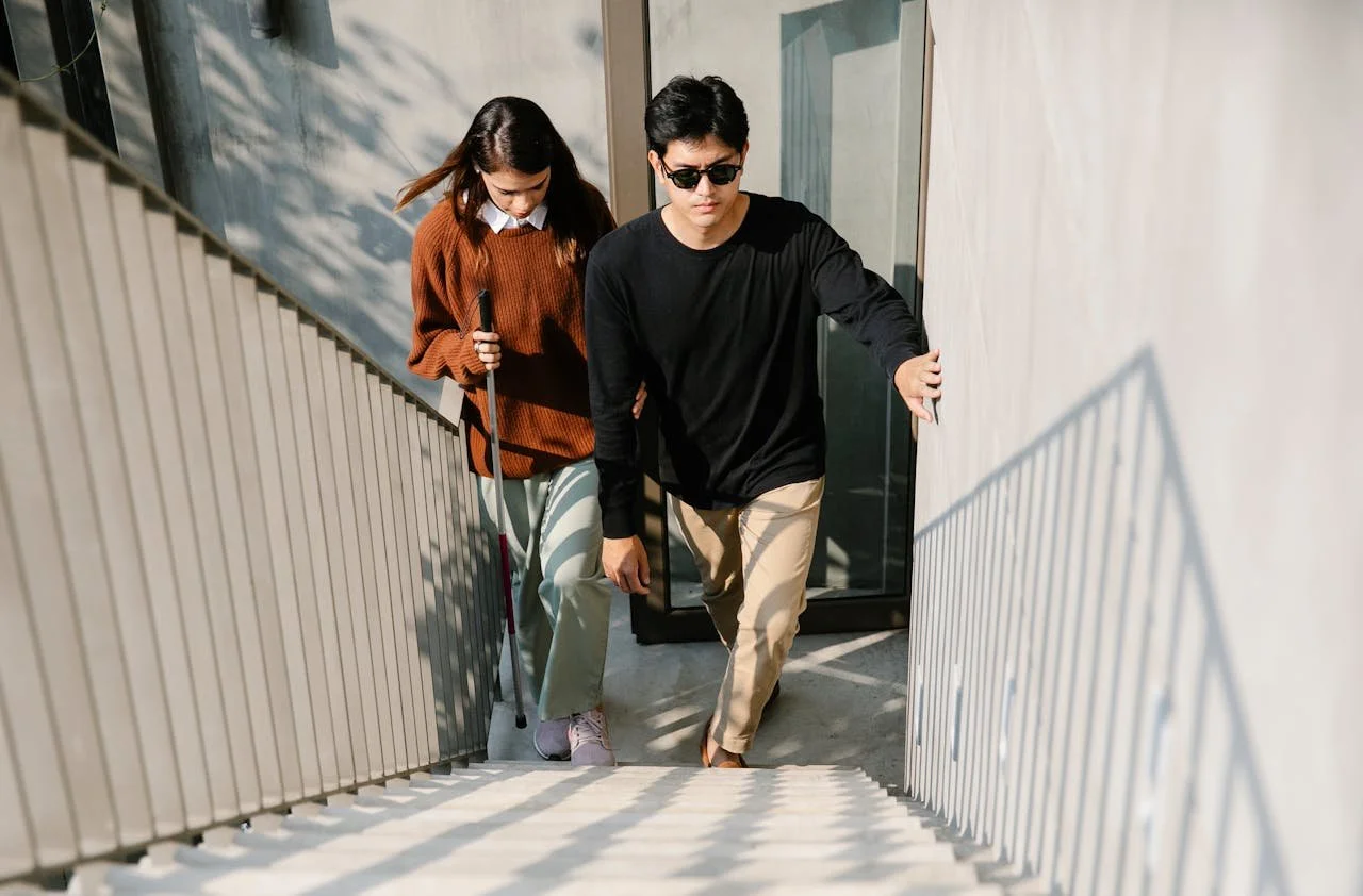 A young man and woman climbing up outdoor stairway, the woman using a cane.