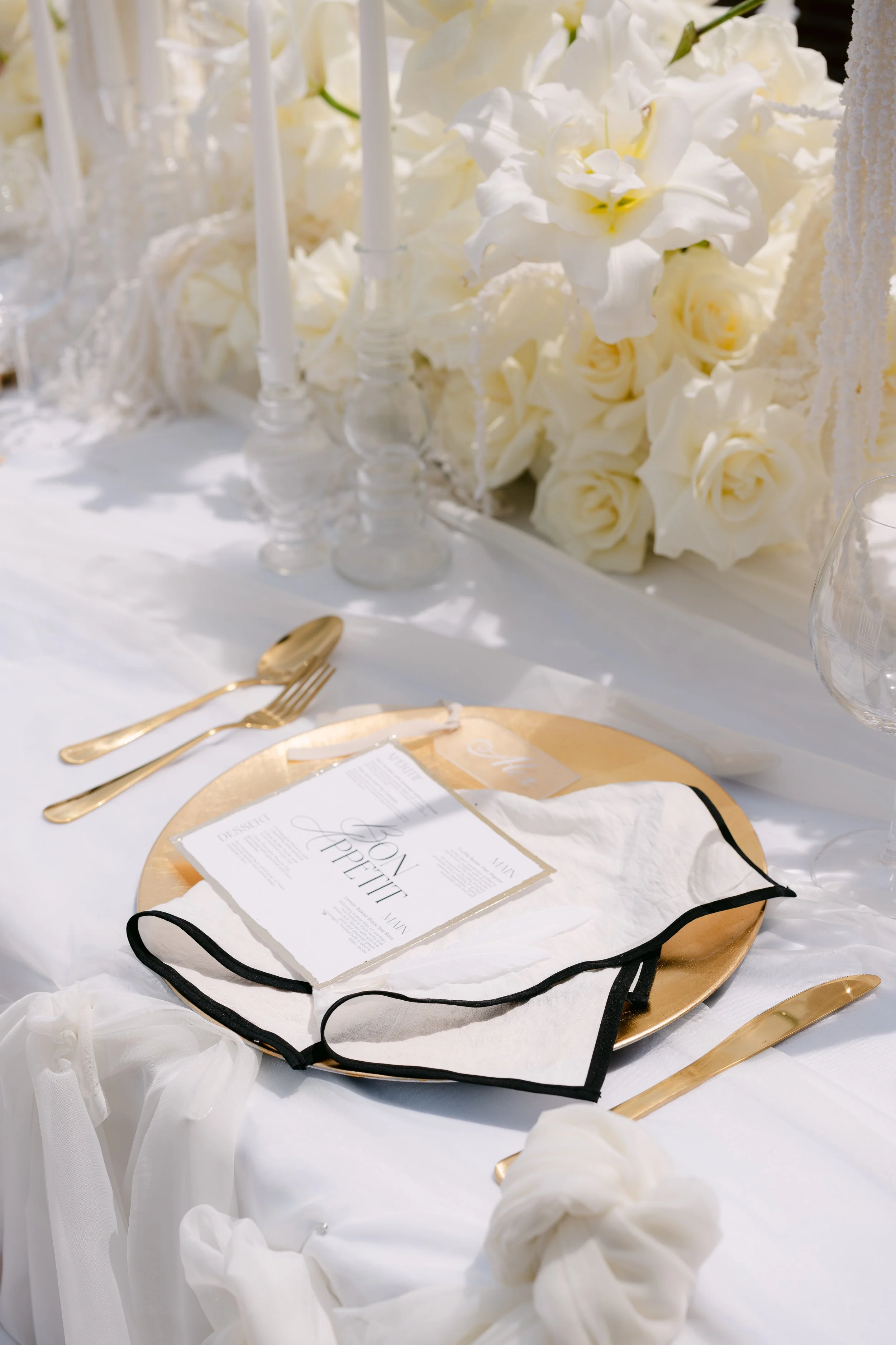 Elegant white and gold wedding table setting with floral centerpiece, candles, menu, and fine china.