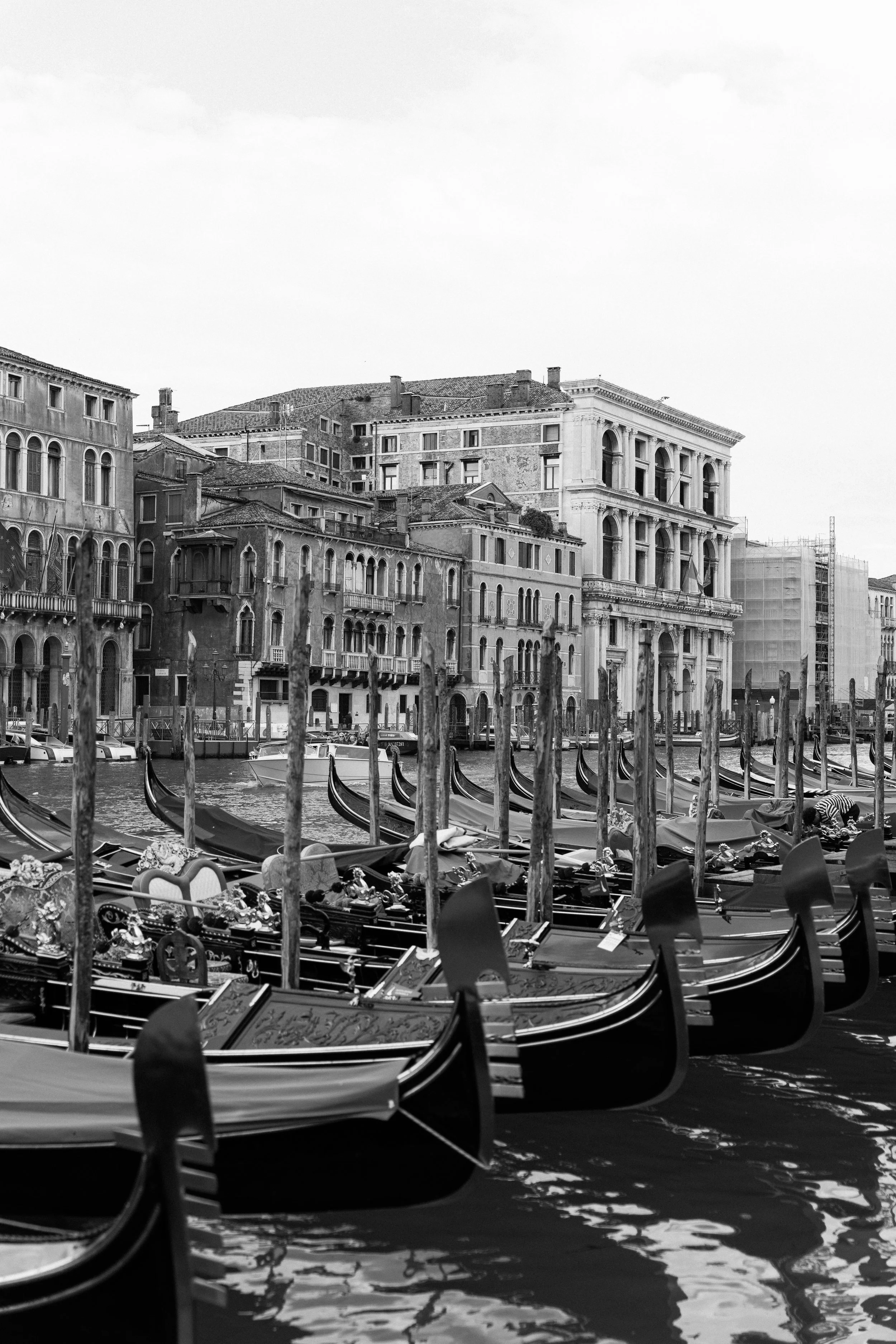 Venetian gondolas docked along a canal with historic buildings in the background, black and white photograph.