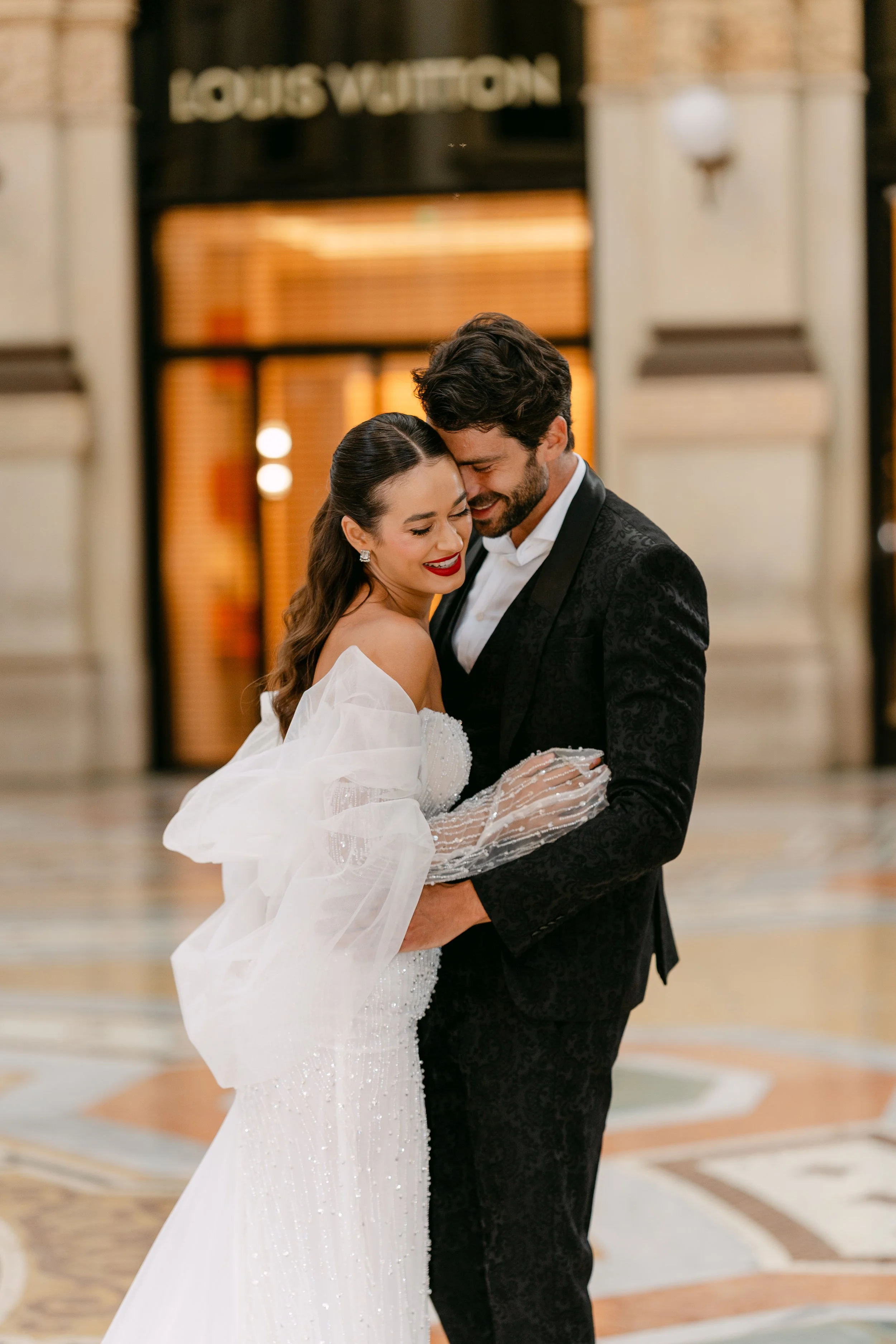 A bride and groom sharing a dance inside a grand hall, smiling joyfully.