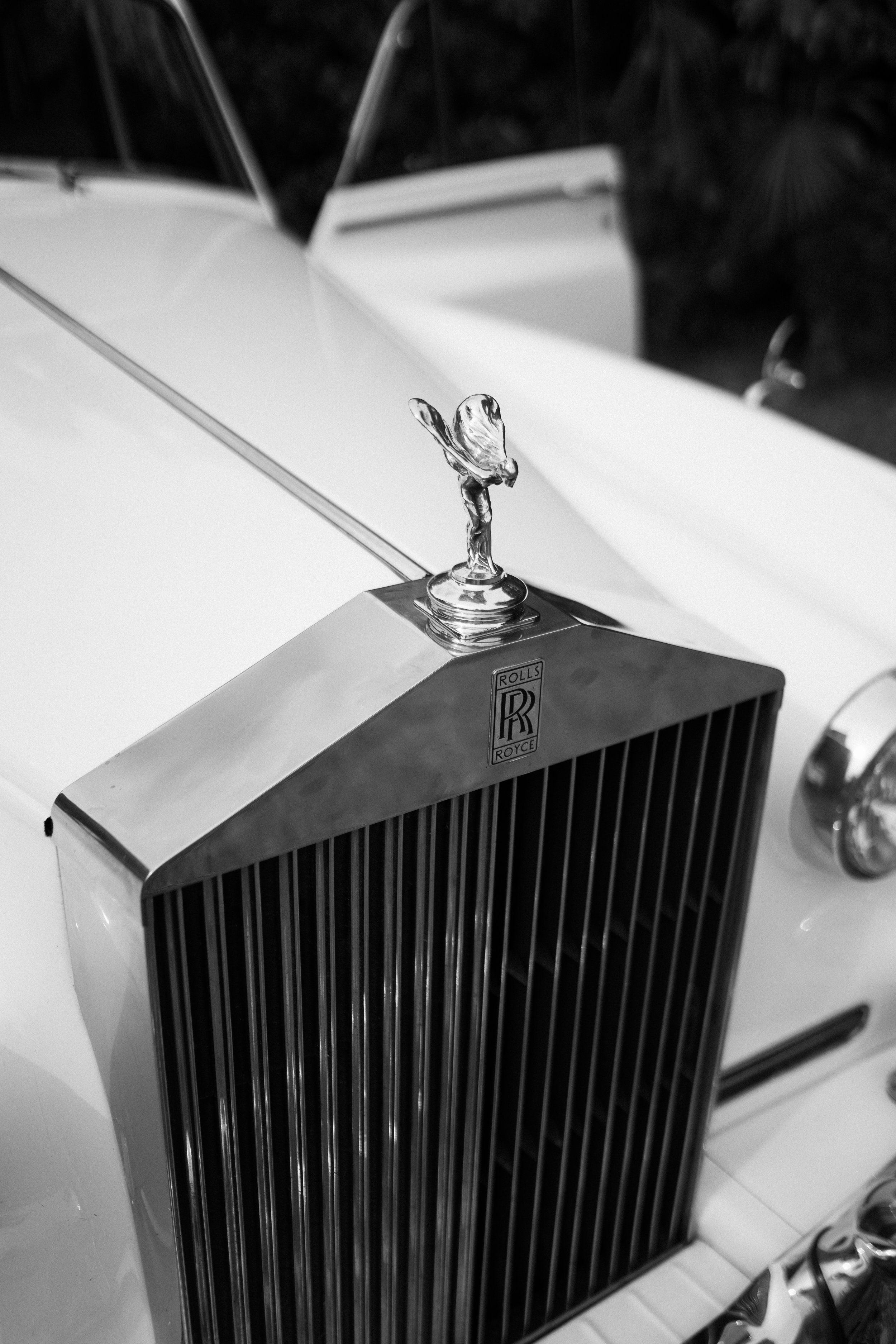 A close-up view of a classic Rolls-Royce car hood ornament, the Spirit of Ecstasy, mounted on the grille of a luxury vehicle.
