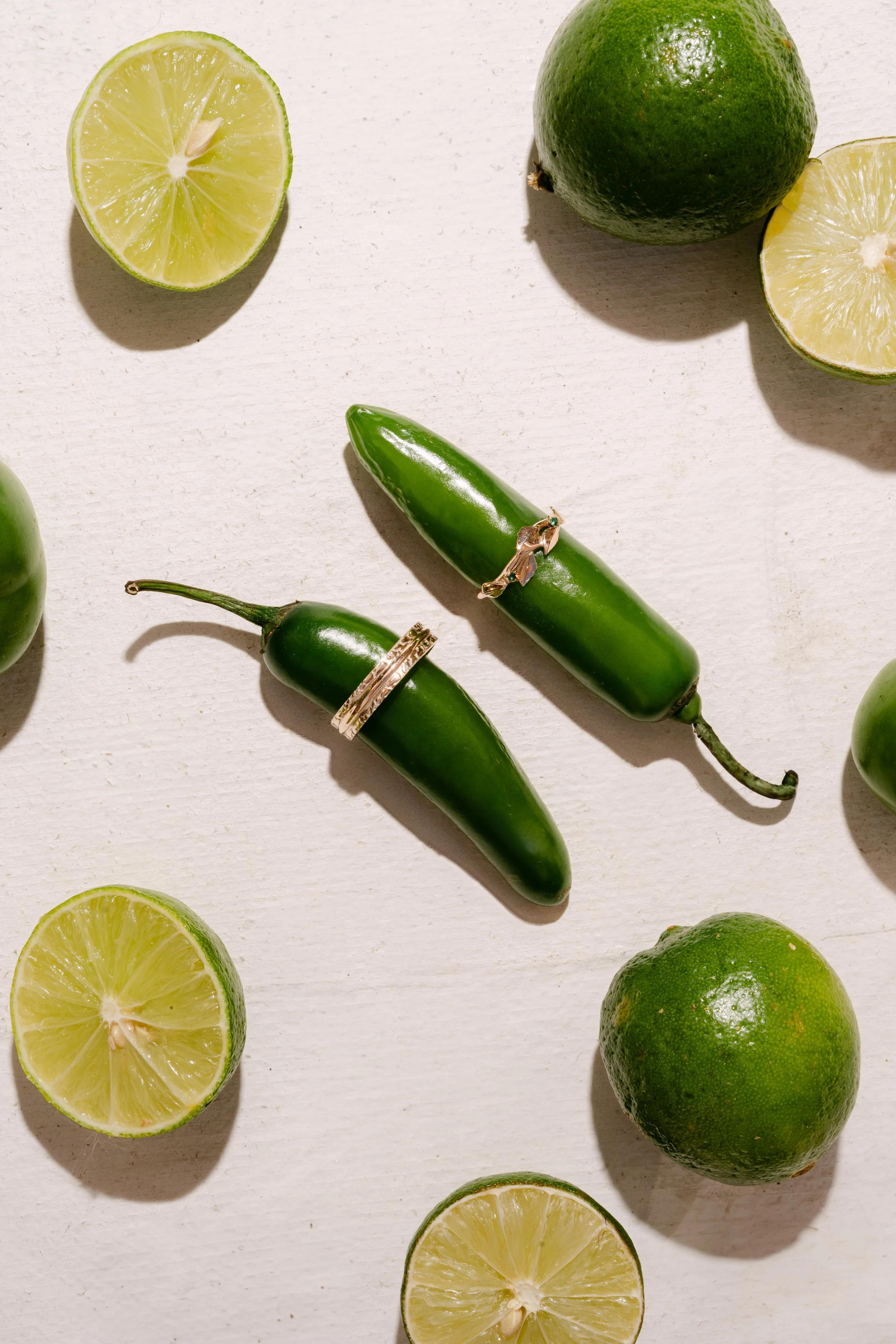 Two jalapeño peppers with rings around them on a white surface, surrounded by halved lemons and whole green limes.