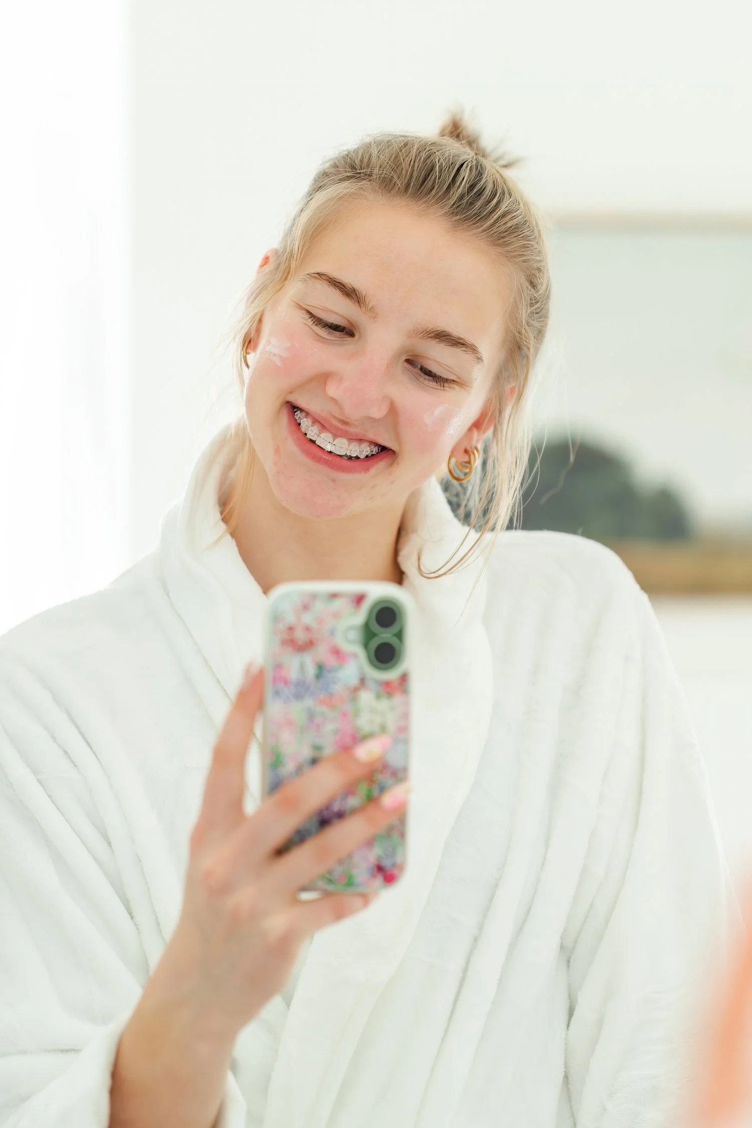 Smiling student in a white sweater looking at a floral phone.