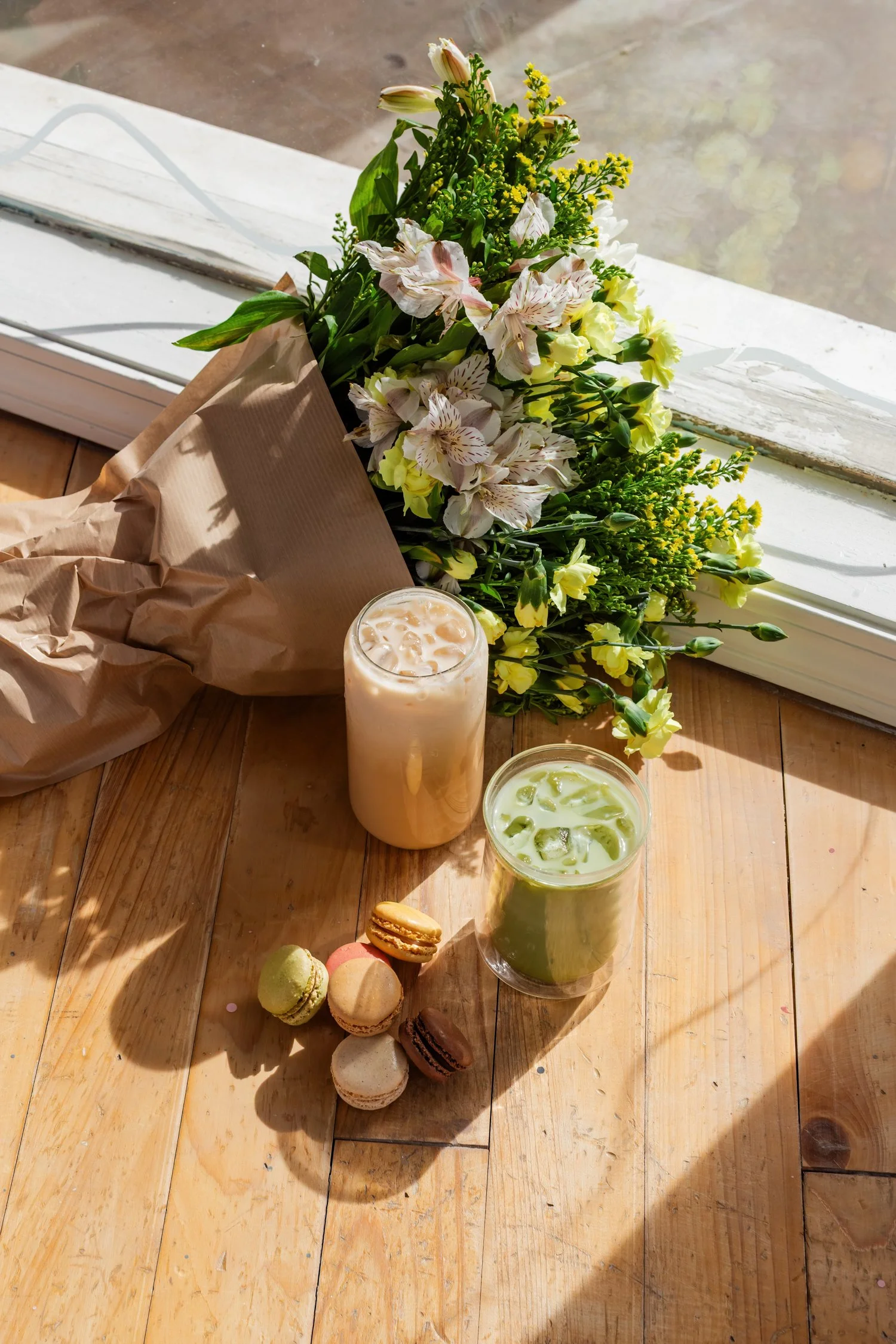 Overhead view of coffee, white flowers, and an open notebook on a wooden table.