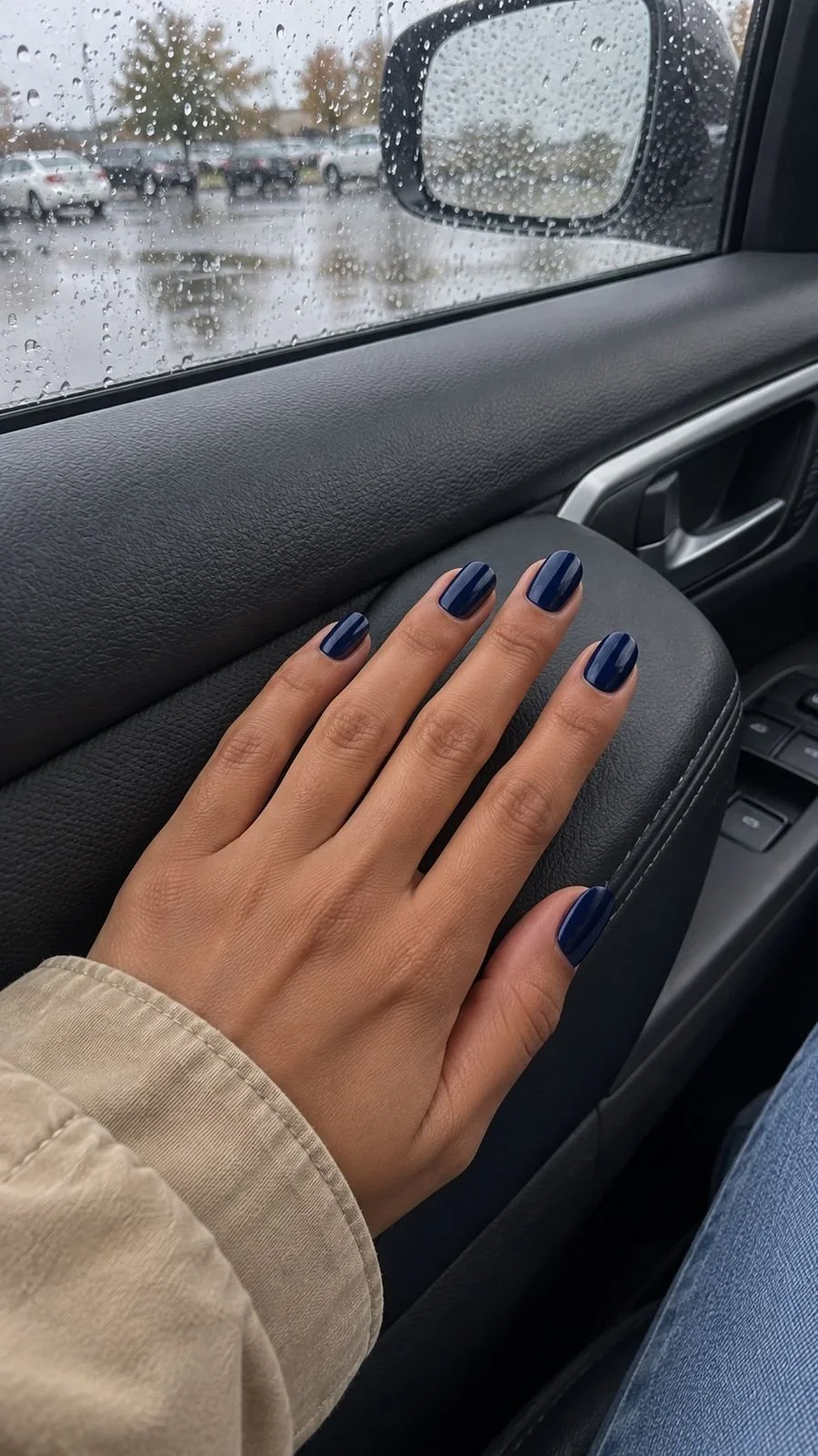 Navy nails on a hand resting on a parked car armrest.