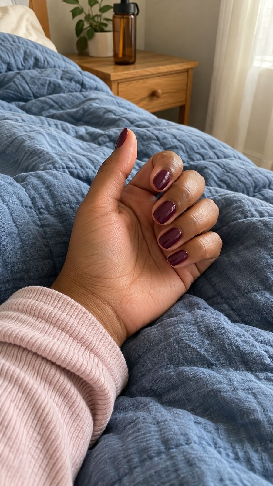 A plum manicure on a loosely curled hand resting on a blue quilt.