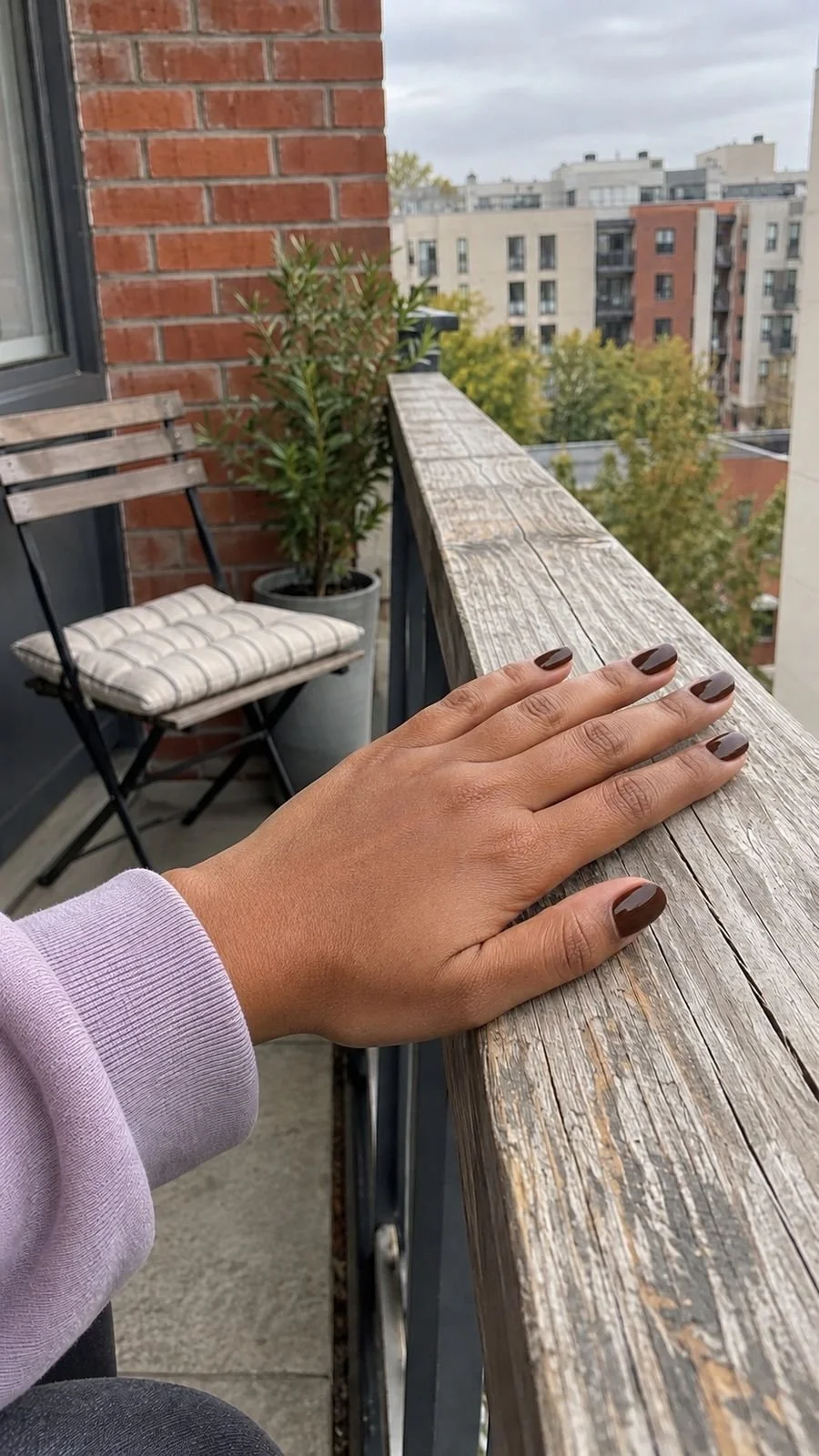 Chocolate brown nails on a relaxed hand resting on a balcony rail.