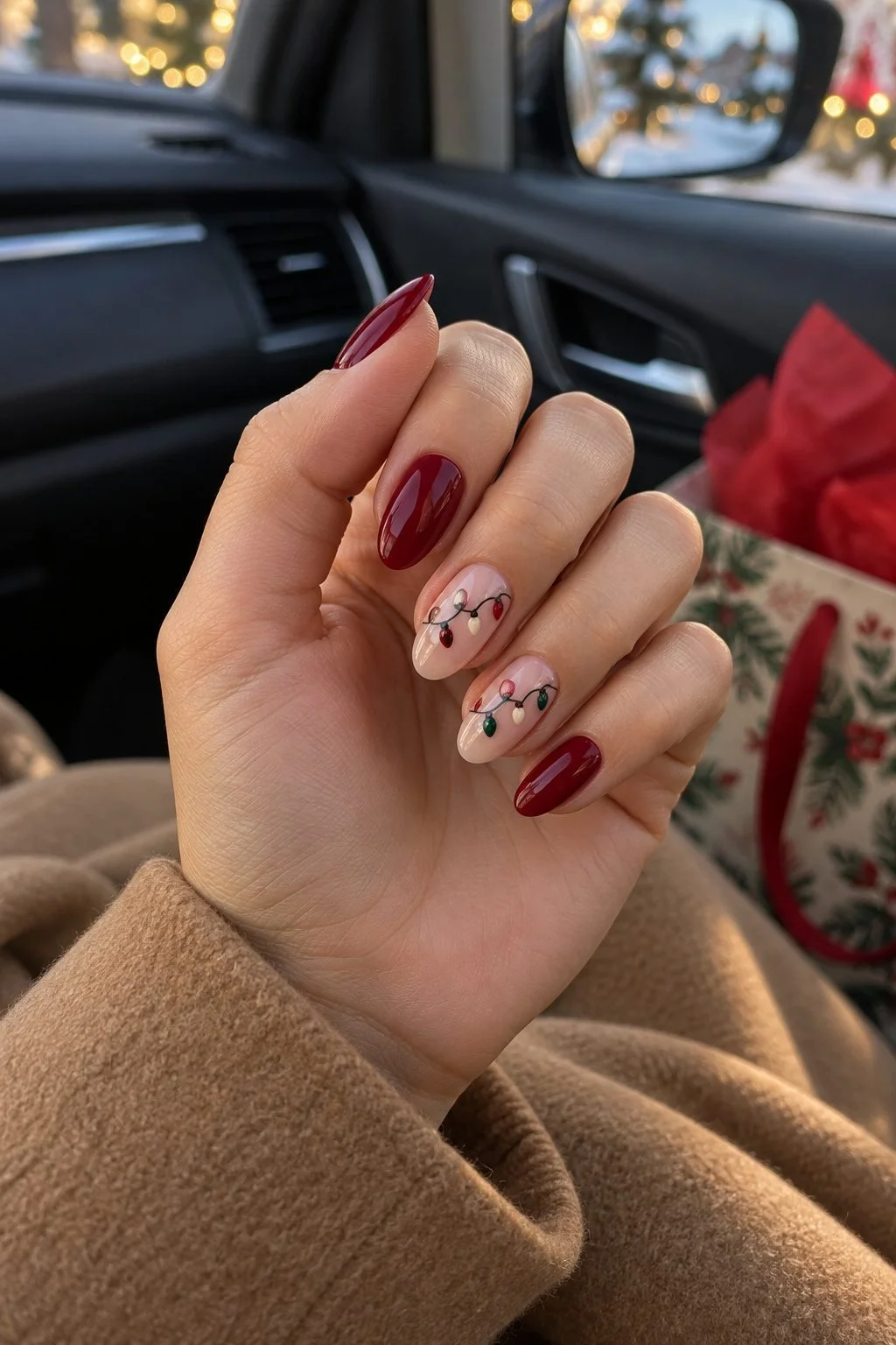 Cranberry nails with tiny Christmas lights on two pale pink accents in a parked car.