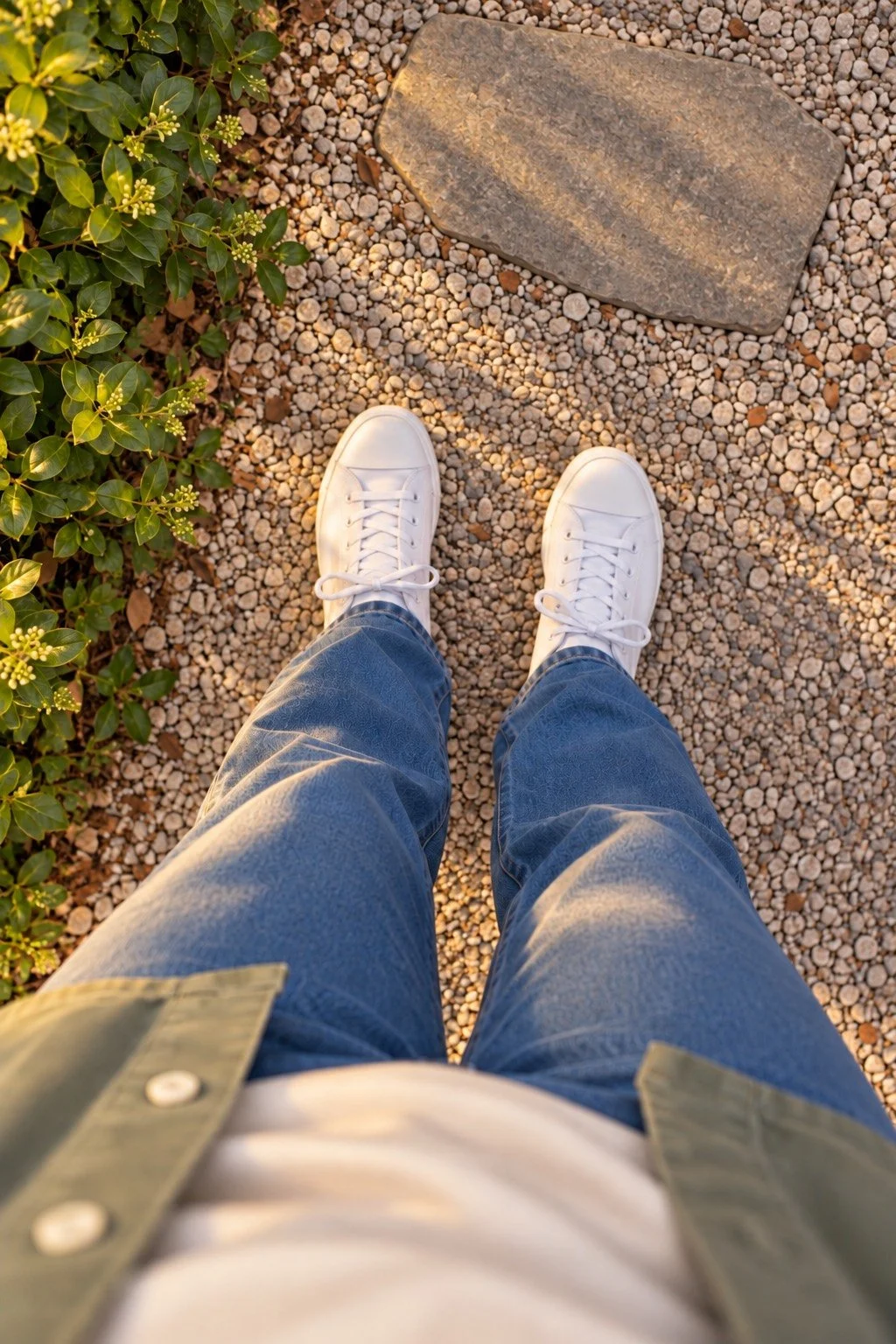 A view down at white sneakers and blue jeans on a sunlit gravel path