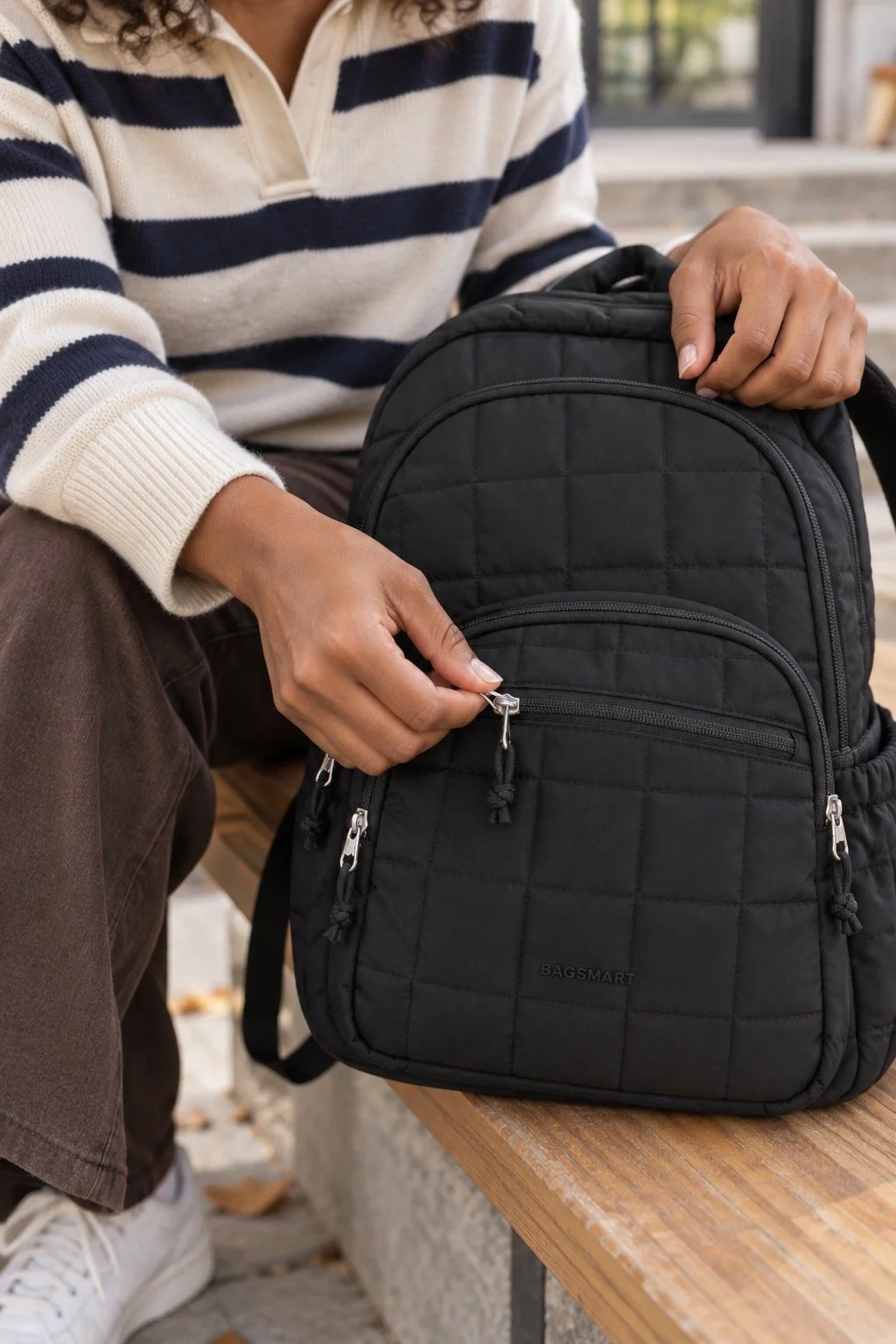 Model C opening the silver front zipper of the black quilted BAGSMART backpack.