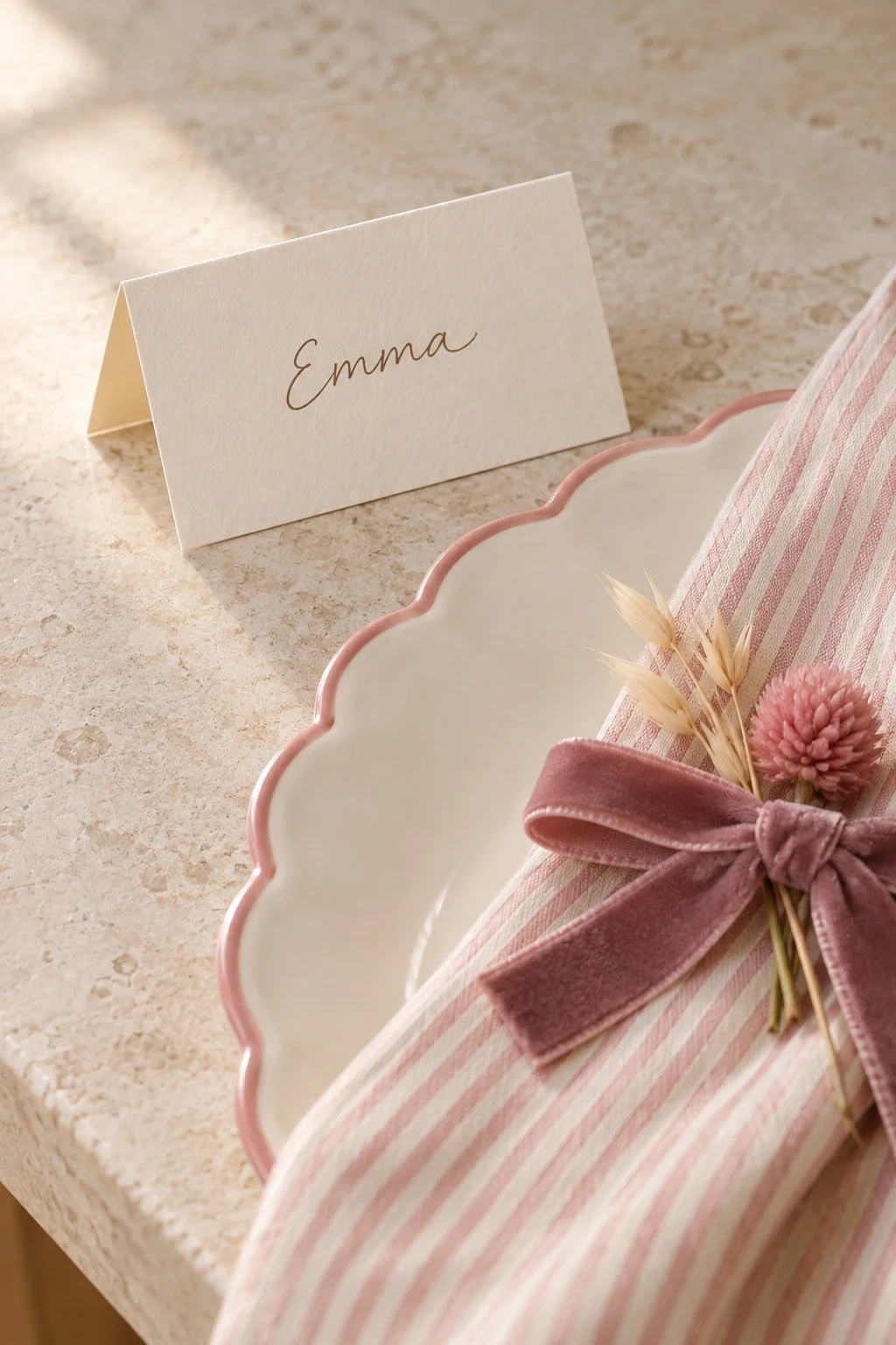 A cream folded card marked Emma stands beside a pink-rimmed plate and ribbon-tied napkin.