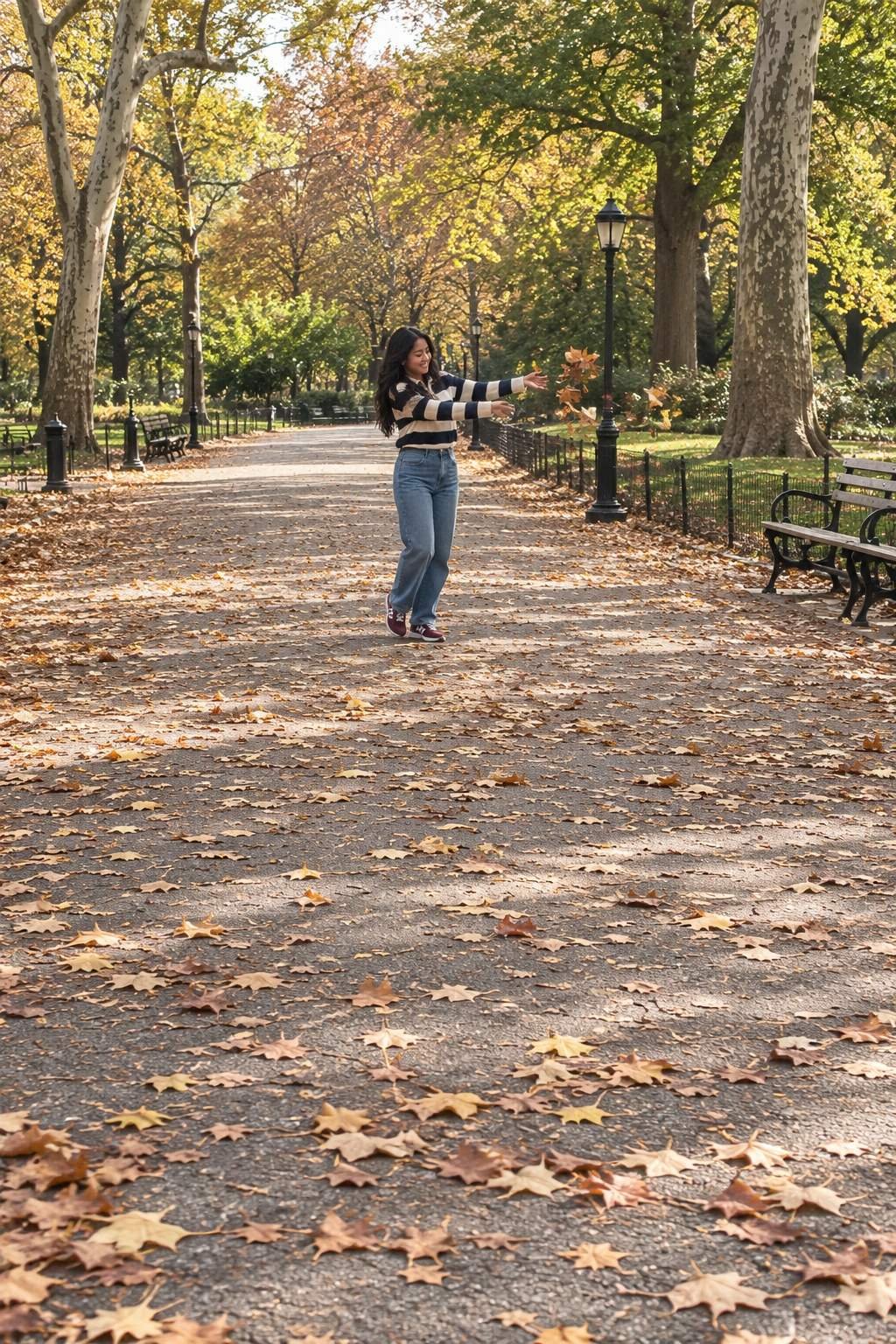 A young woman tosses red and gold leaves on a park path.
