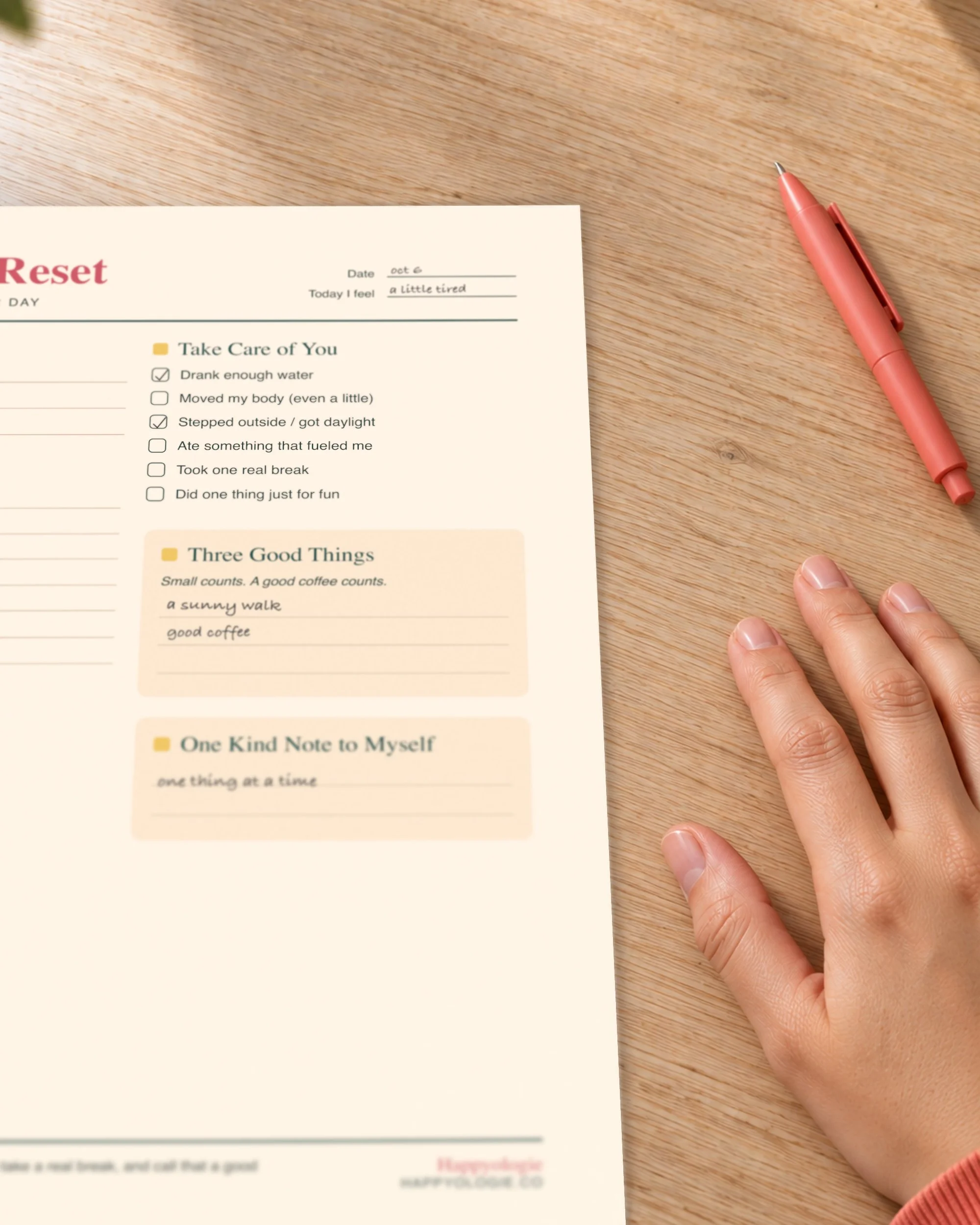 A hand and pen beside the self-care section of The Daily Reset planner.