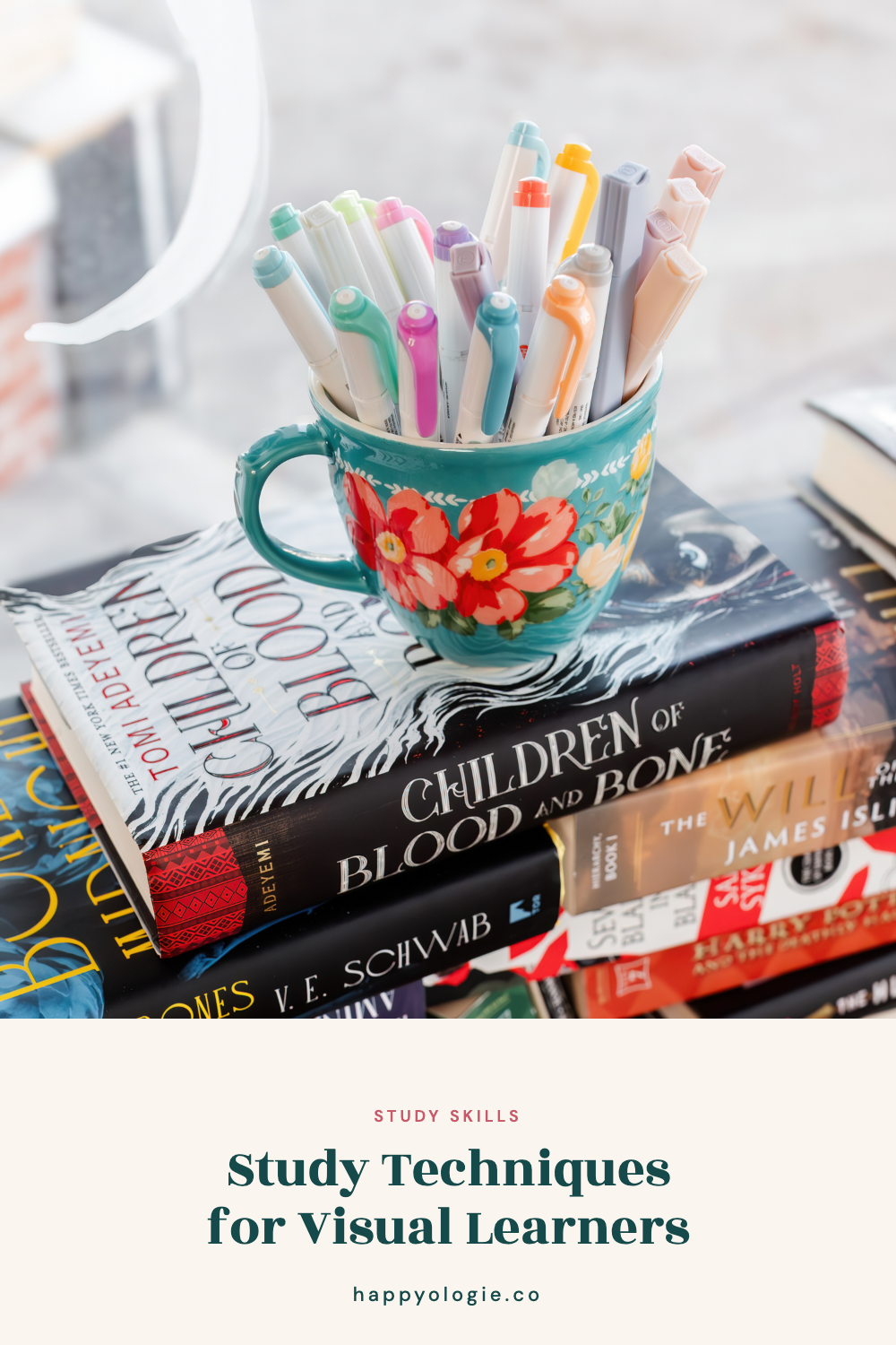 Colorful markers in a floral mug resting on a stack of books.