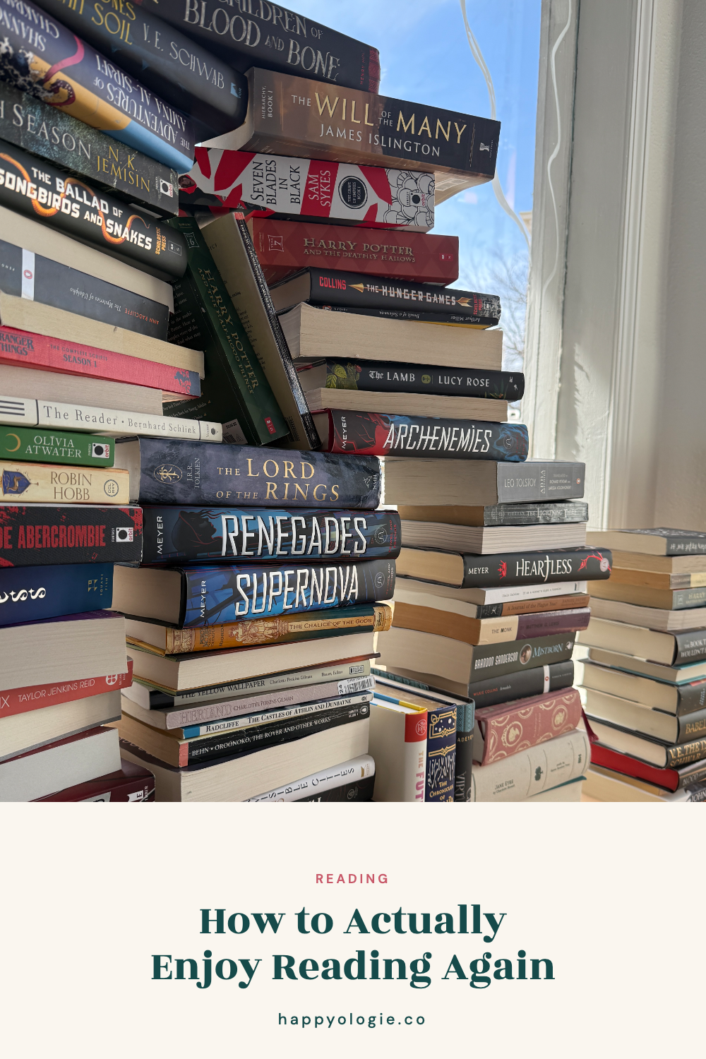 Stacks of books beside an open book in front of a sunny window.