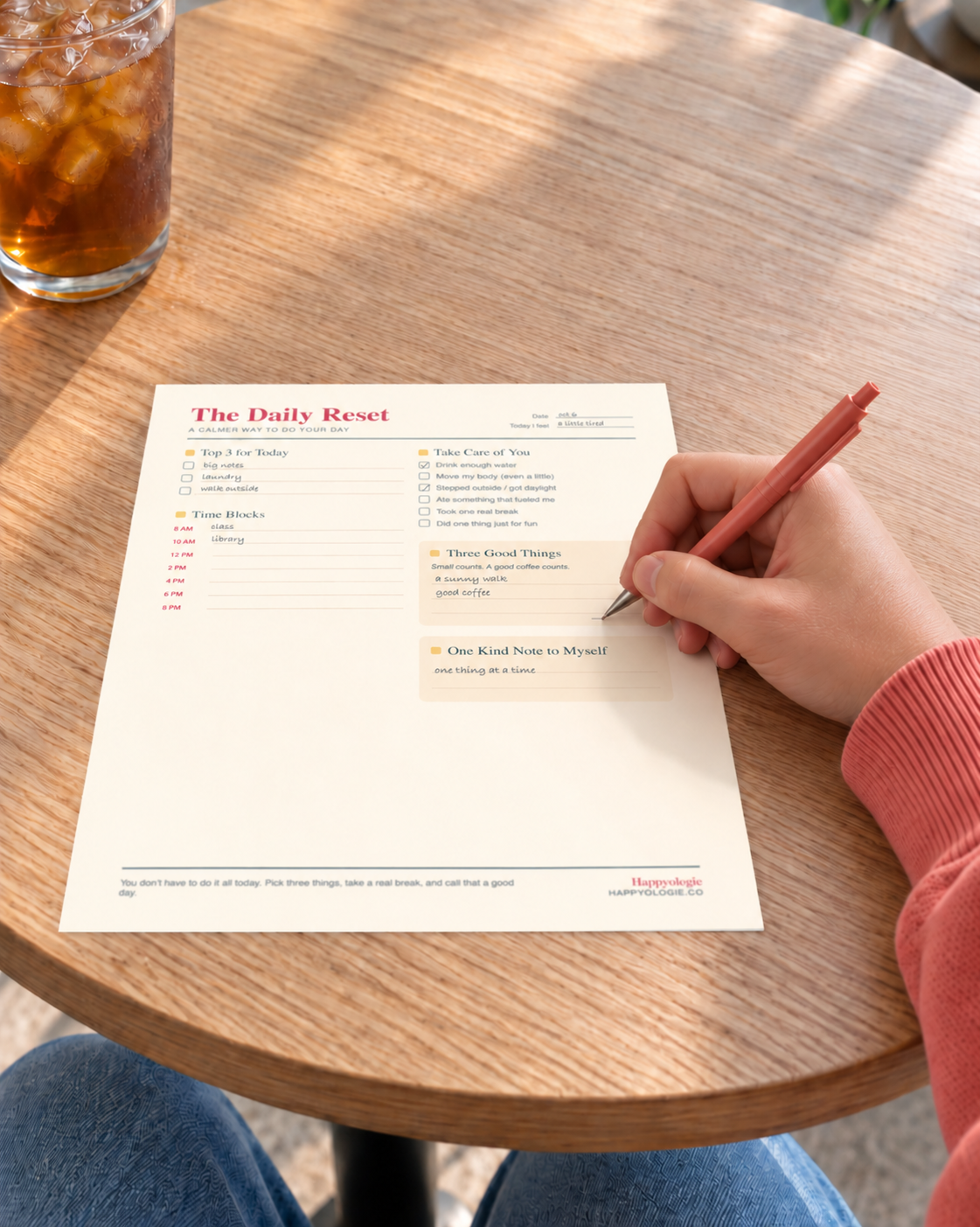 A hand writing on The Daily Reset planner at a café.