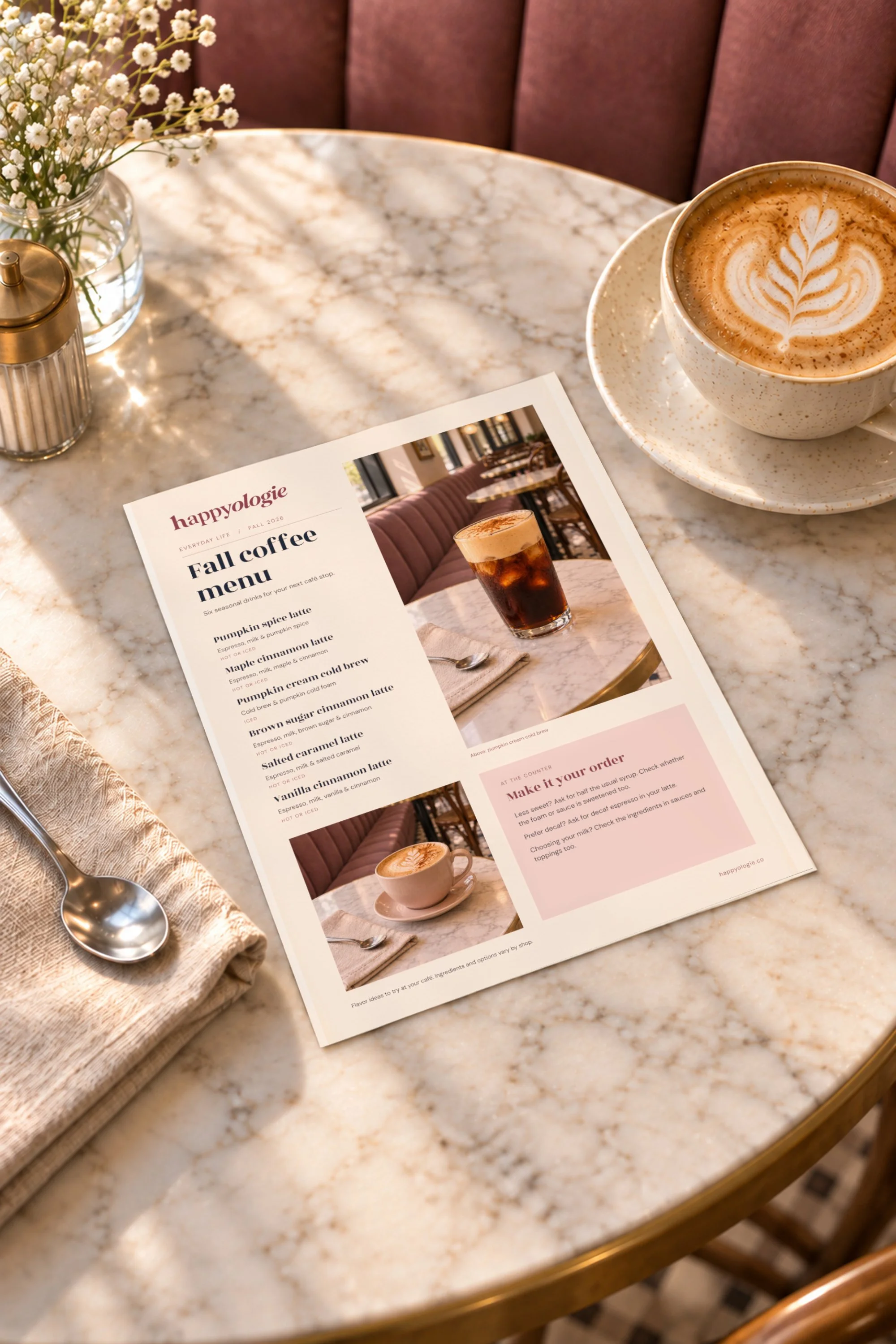 Happyologie Fall Coffee Menu beside a latte and flowers on a marble café table.