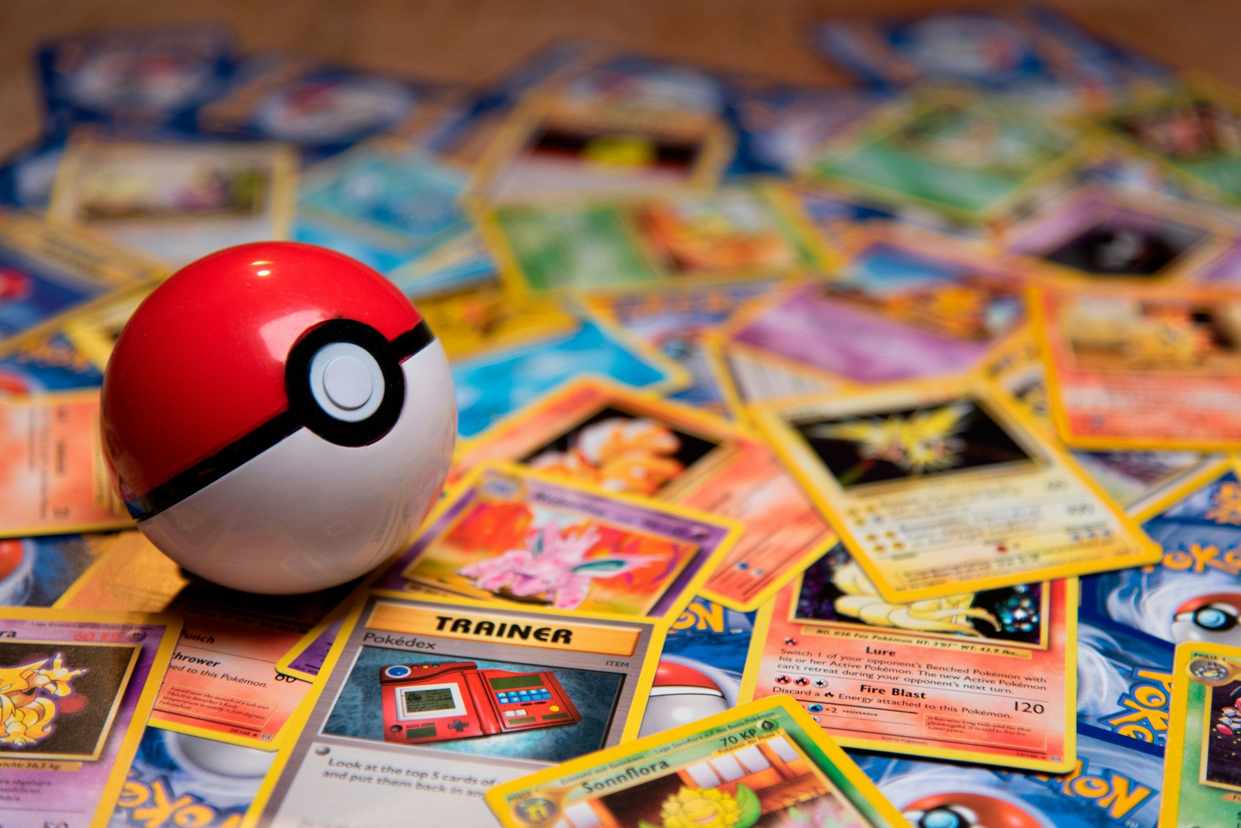 A red and white Poké Ball rests on a scattered pile of Pokémon trading cards.