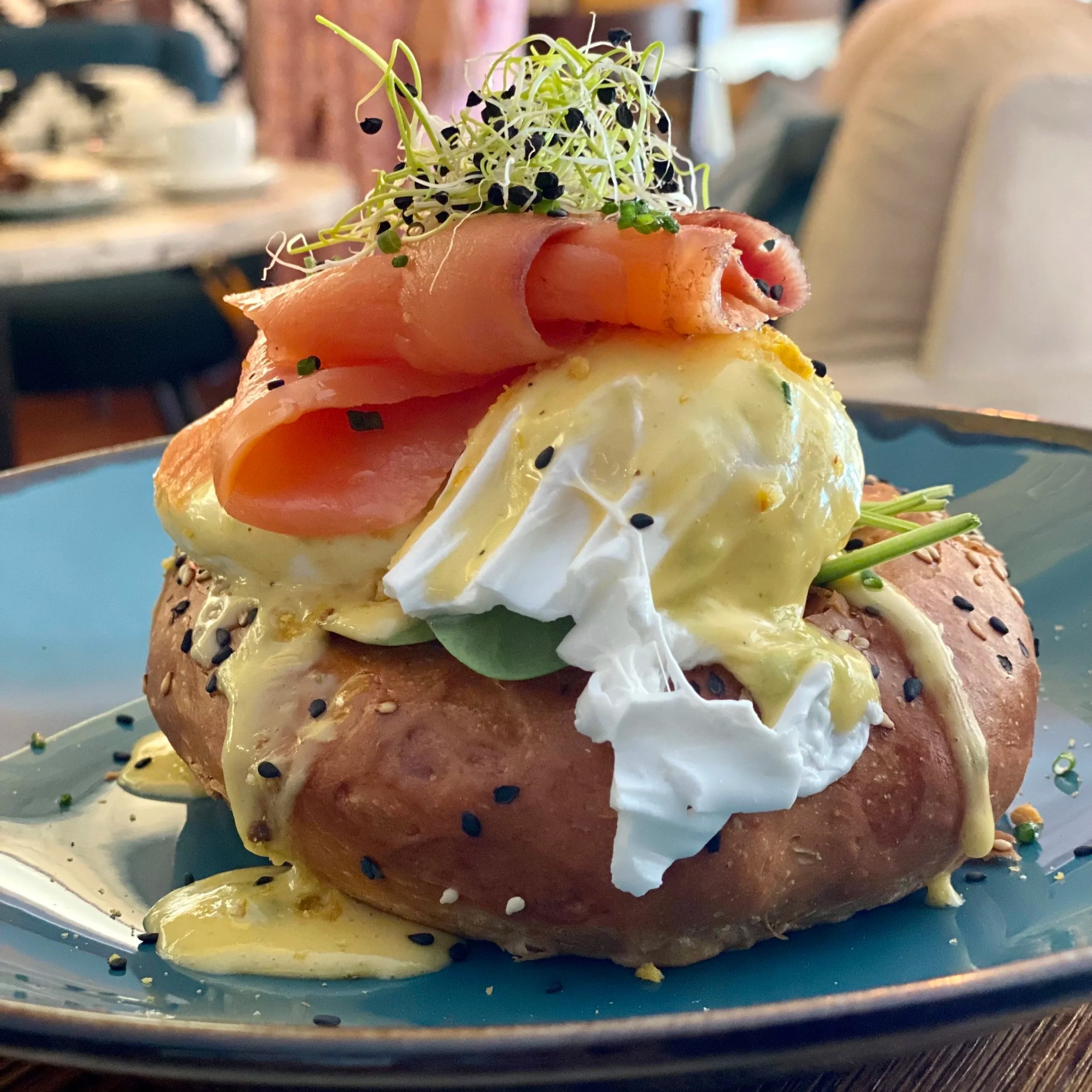 Huevos pochados sobre un brioche, con jamón, Salomon o bacon, microgreens y semillas negras condimentadas.