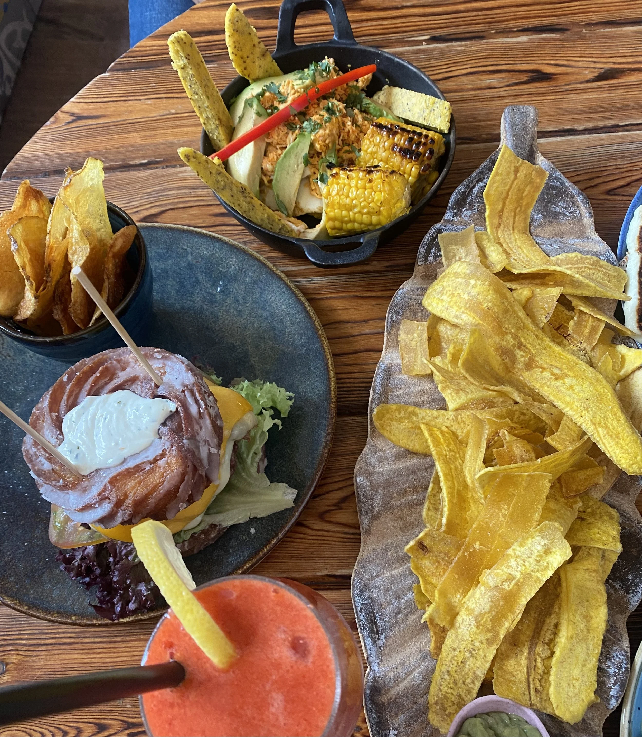 Plato de tacos, papas fritas, cebolla frita, ensalada con maíz, aguacate y salsa, y una bebida de color rojo con limón.