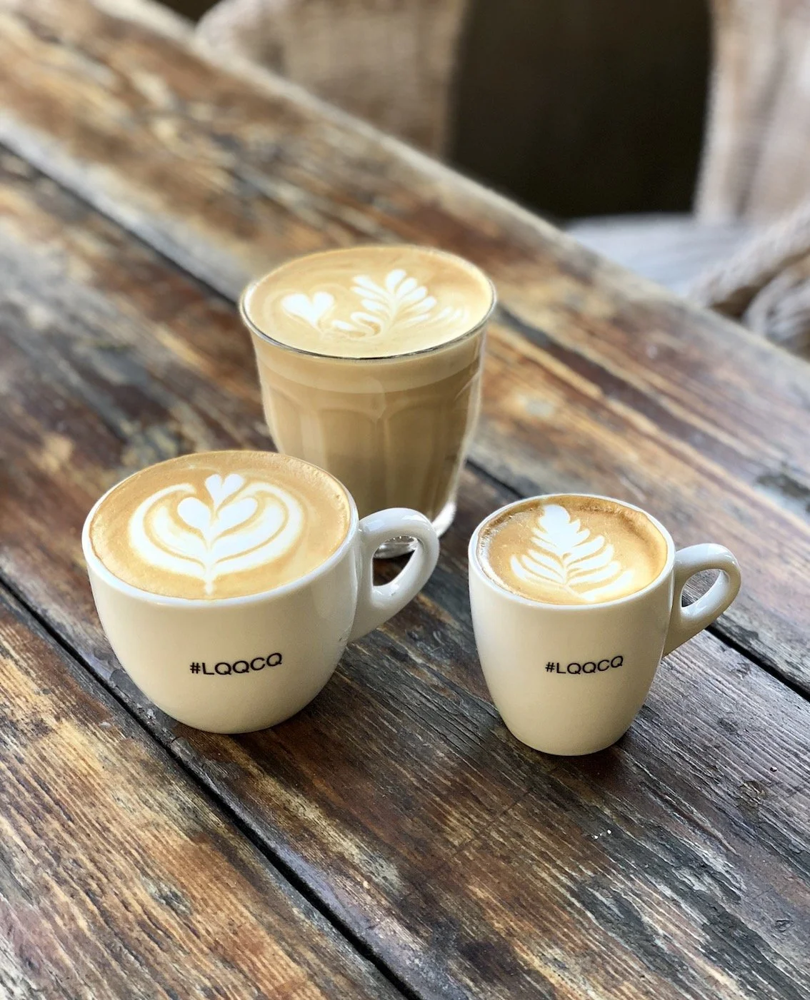 Tres tazas de café con arte en la leche sobre una mesa de madera rústica.