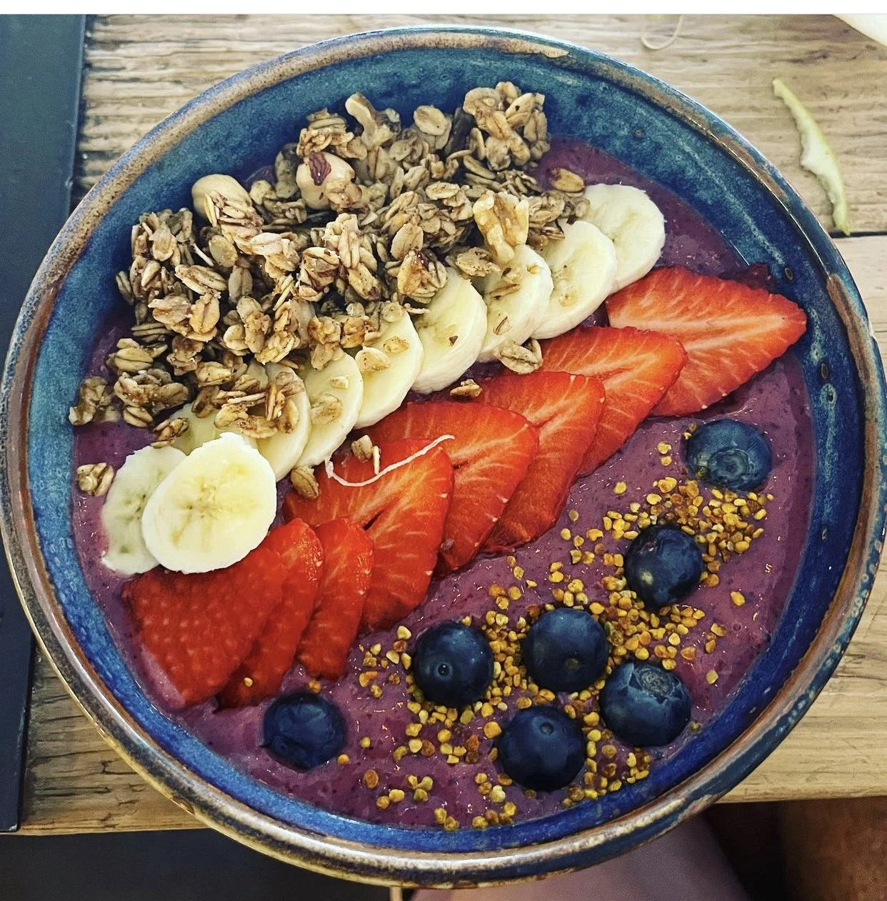 Un tazón con baya de acai, rodajas de plátano, fresa, arándanos y semillas de miel, y granola en la parte superior.