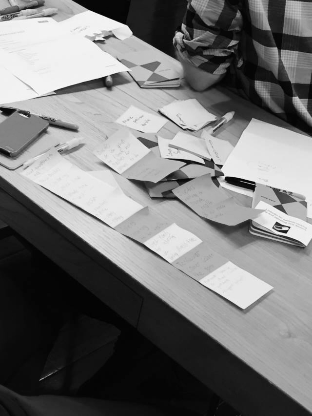 A desk with scattered notes, papers, some notebooks, pens, and highlighters, with a person partially visible.