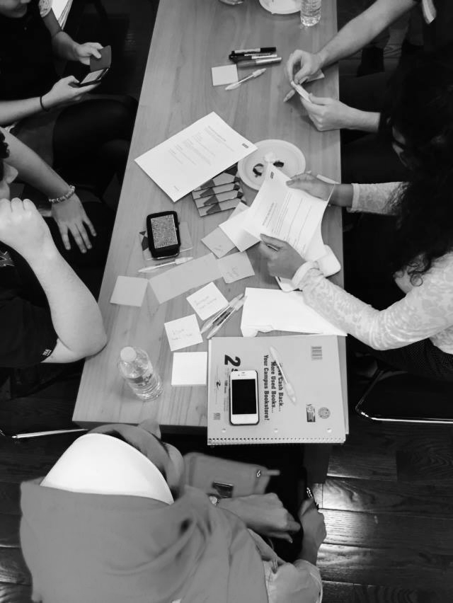 People working on a table with papers, notebooks, pens, and smartphones in a meeting or study session.