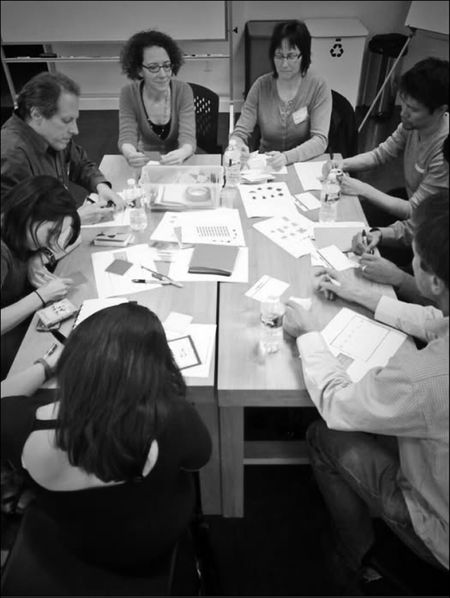 Group of people sitting around a rectangular table during a meeting or workshop, looking at papers and engaging in discussion.