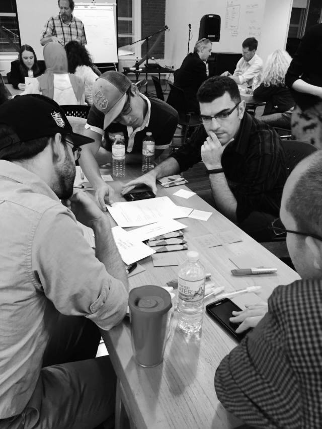 People sitting around a table working on papers and using smartphones in a meeting or workshop.