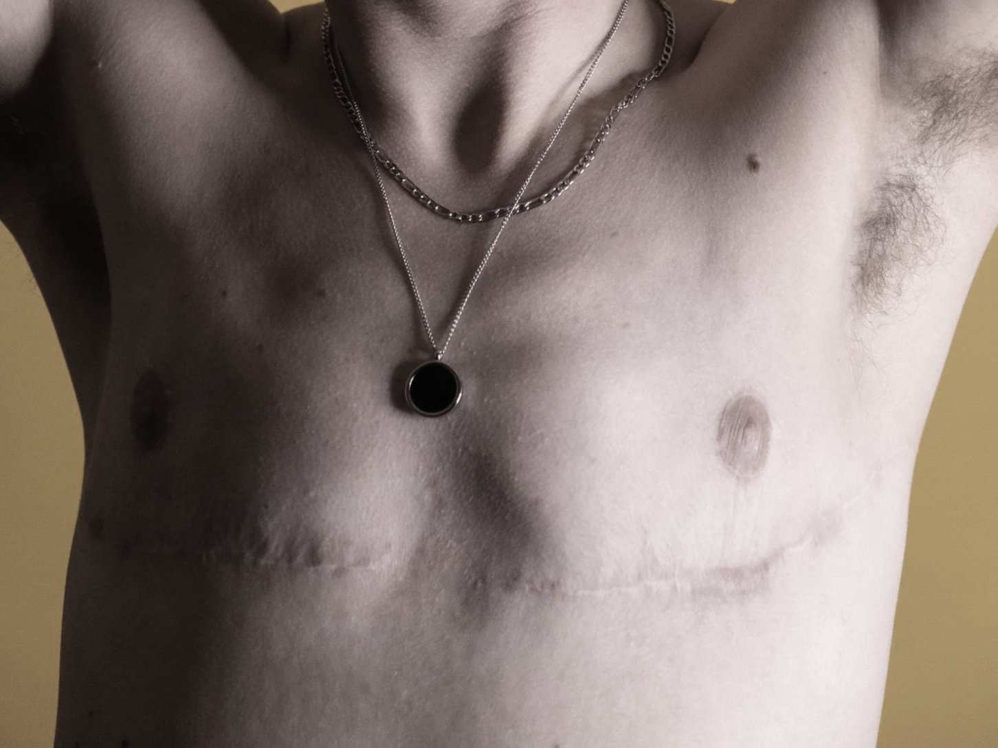 Close-up of a shirtless person wearing two necklaces, one with a black pendant and the other a silver chain.