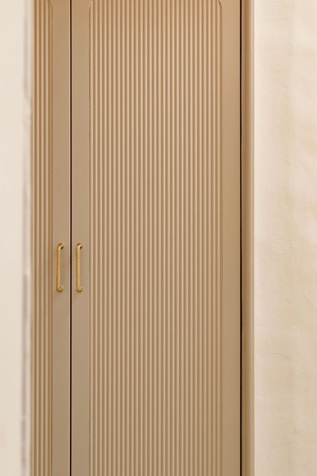 A beige closet with ribbed doors and gold handles.