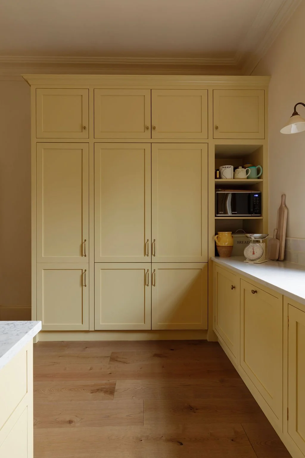 Yellow kitchen cabinets with a microwave, dishes, and a scale on the counter, light wood flooring, and a small countertop.