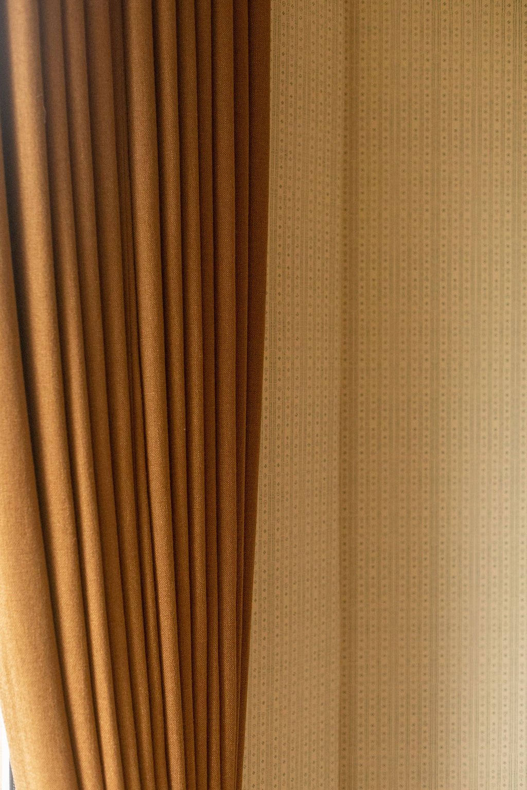 Close-up of heavy mustard-coloured curtains next to a wallpapered wall with a subtle dotted pattern.