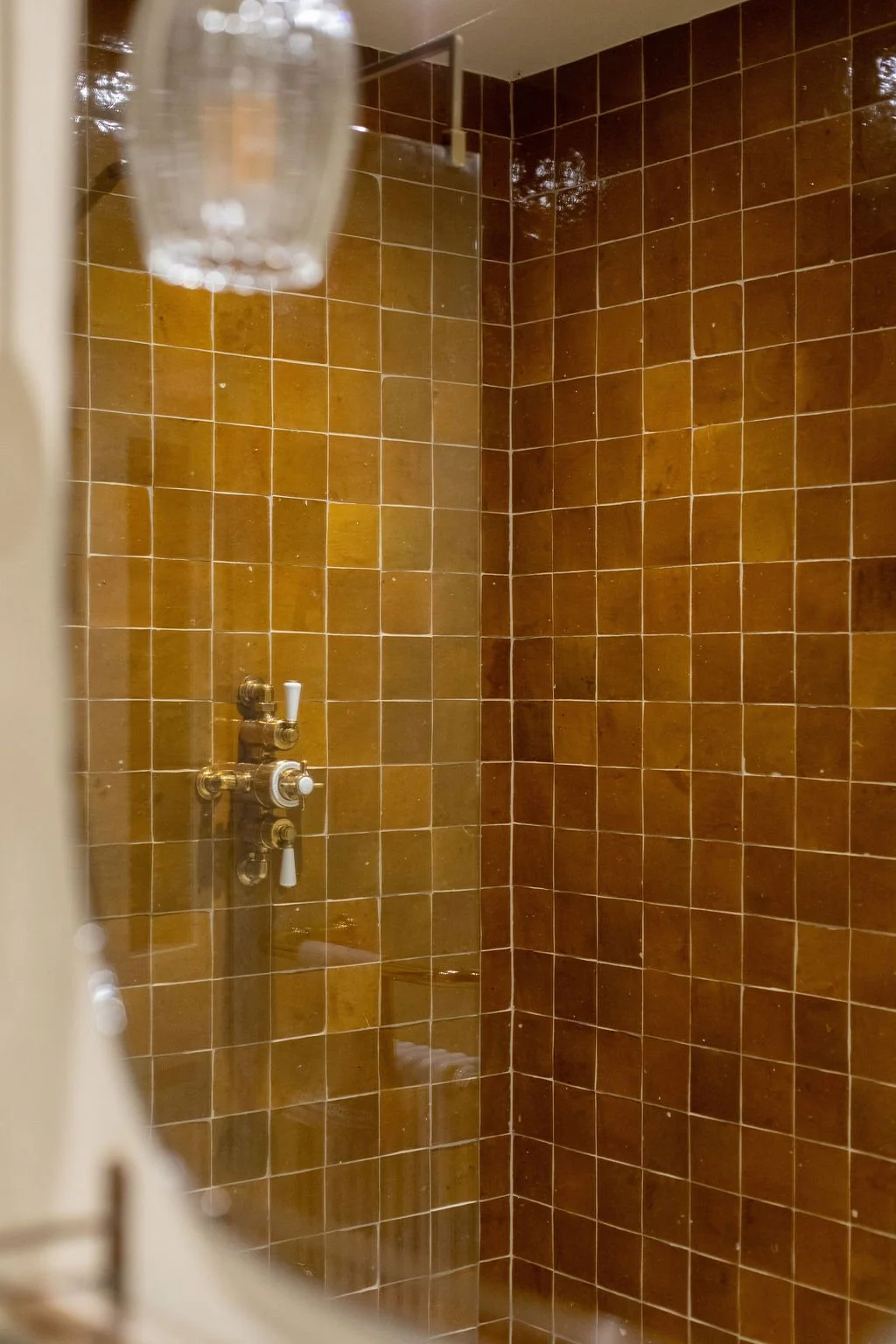 A corner shower with brown tiled walls and wall-mounted brass shower fixtures.