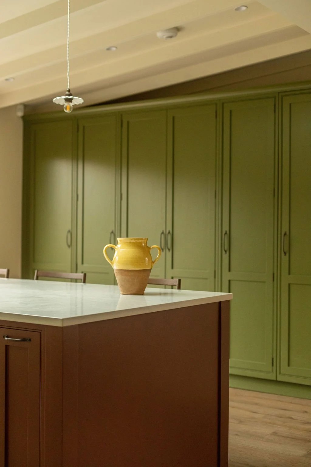 A yellow and brown ceramic vase on a red kitchen island with green cabinets in the background.