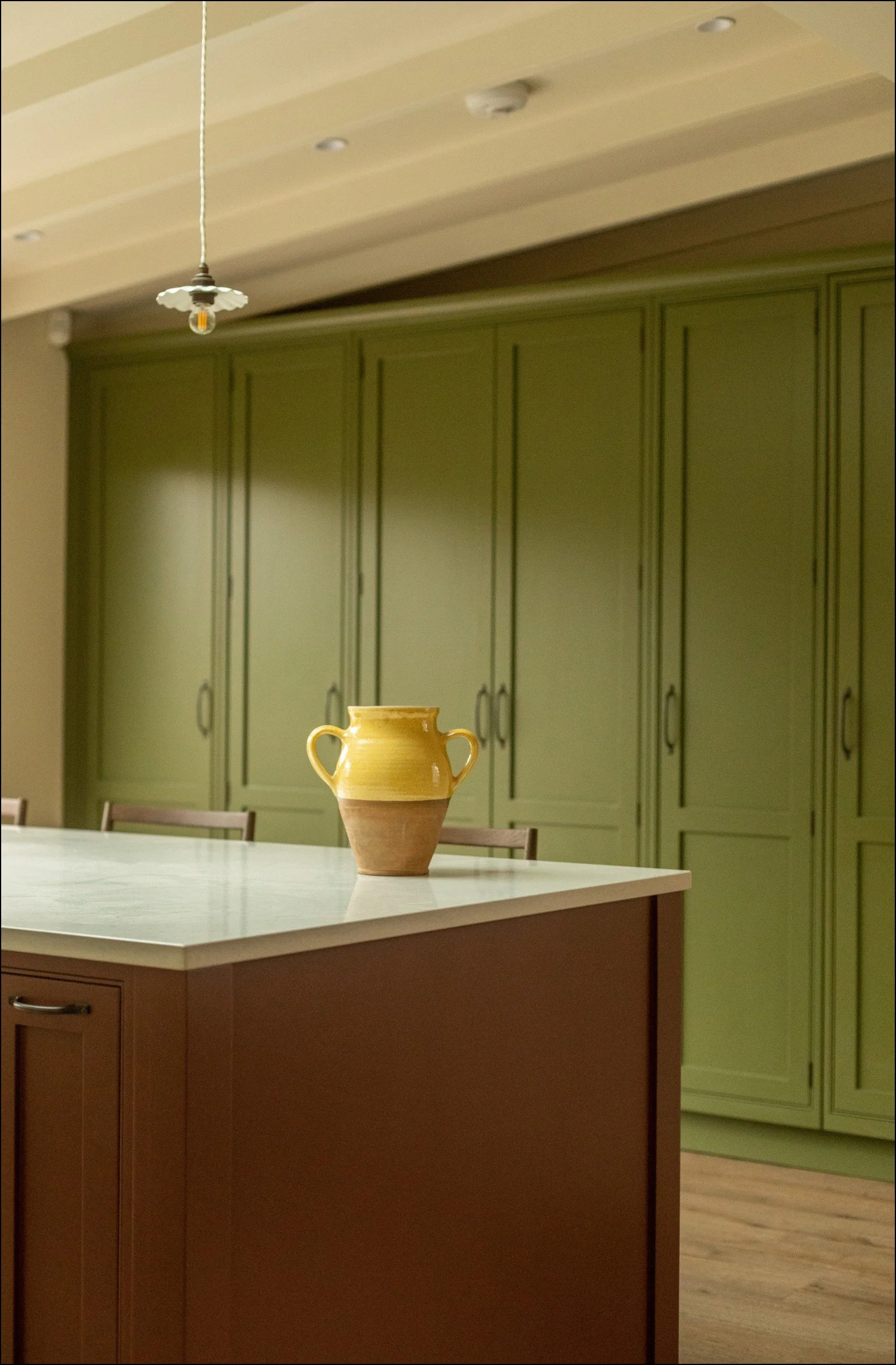 A yellow and brown ceramic vase on a red kitchen island with green cabinets in the background.