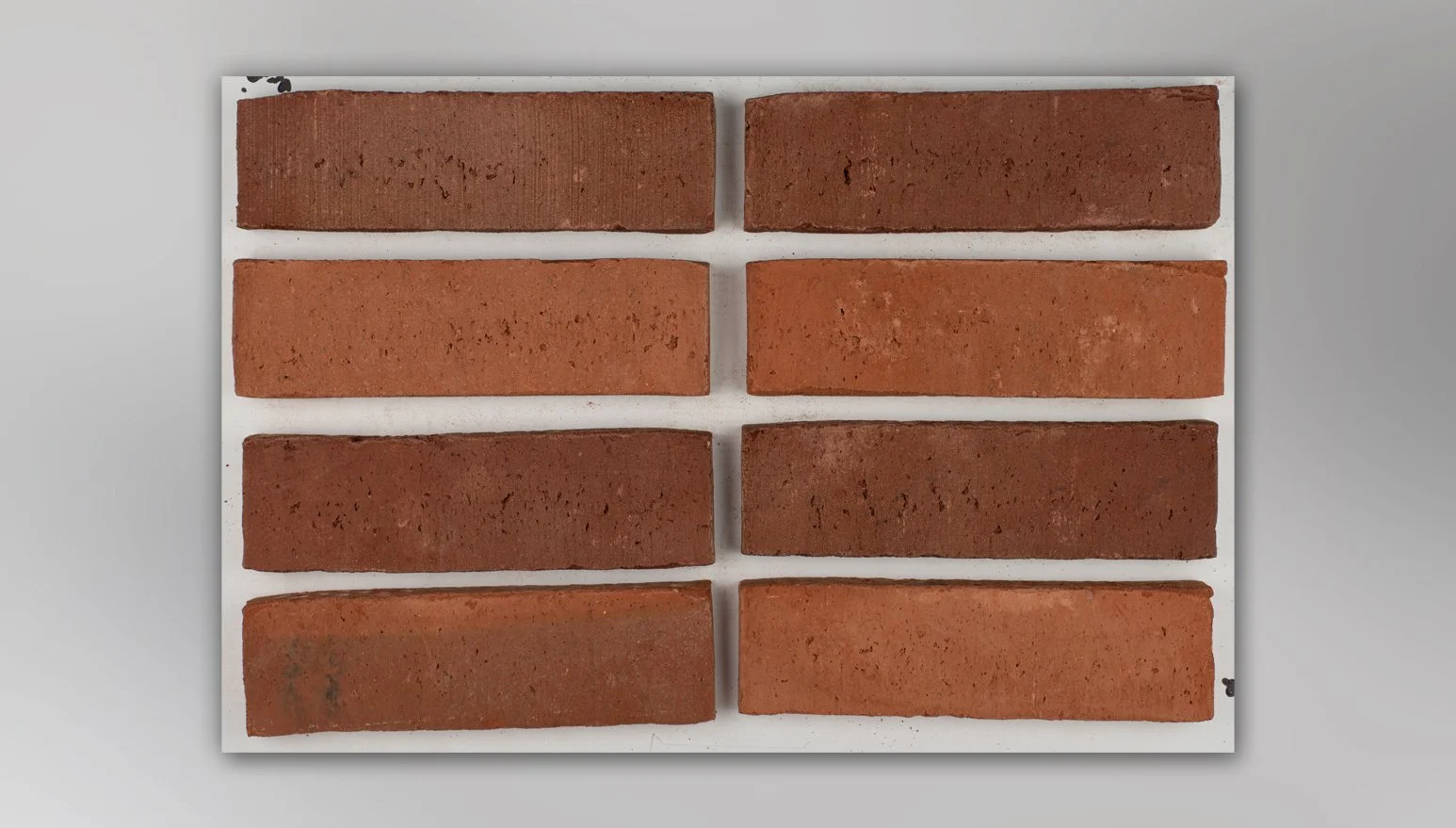 Eight bricks arranged in four rows with four bricks each, placed on a white board against a gray background.