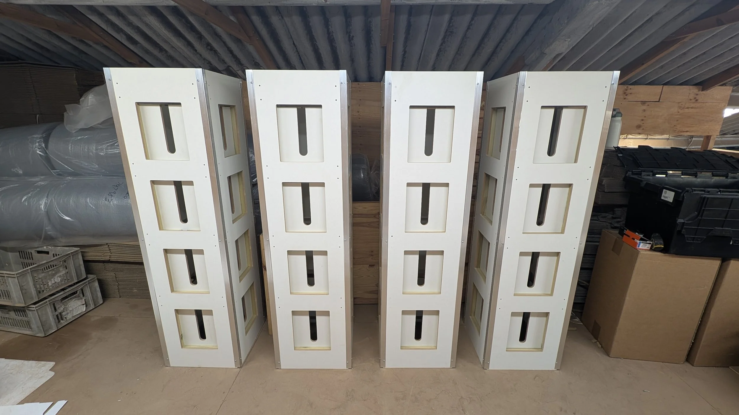 Stacked white wooden panels with rectangular cutouts, leaning against a wall in a storage room.