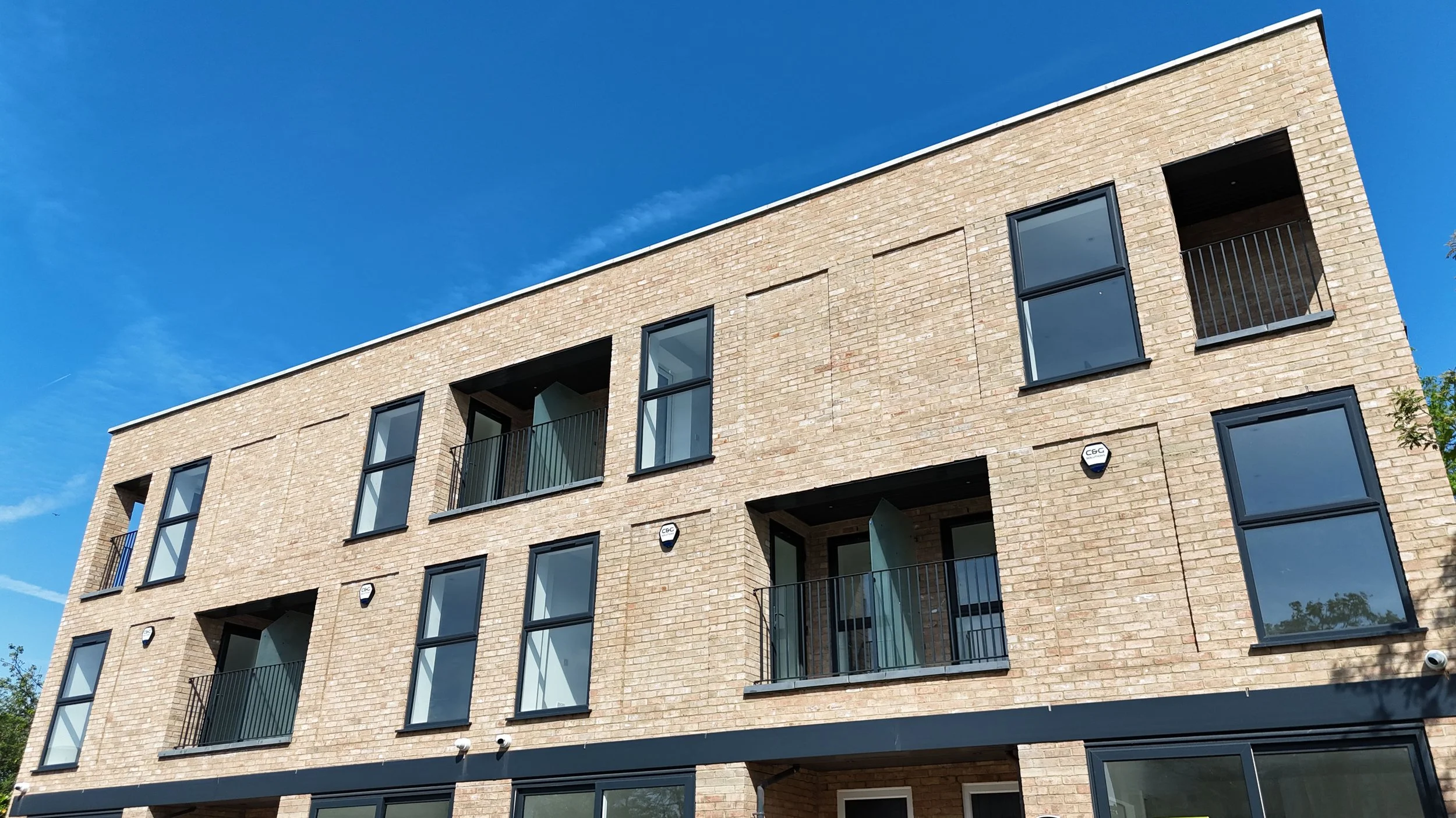 Modern brick apartment building with multiple large windows and small balconies against a blue sky.