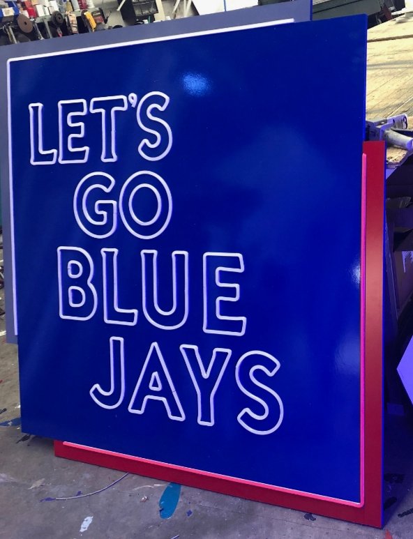 Blue sign with white neon outline text that says "Let's Go Blue Jays" in a sports arena or store setting.