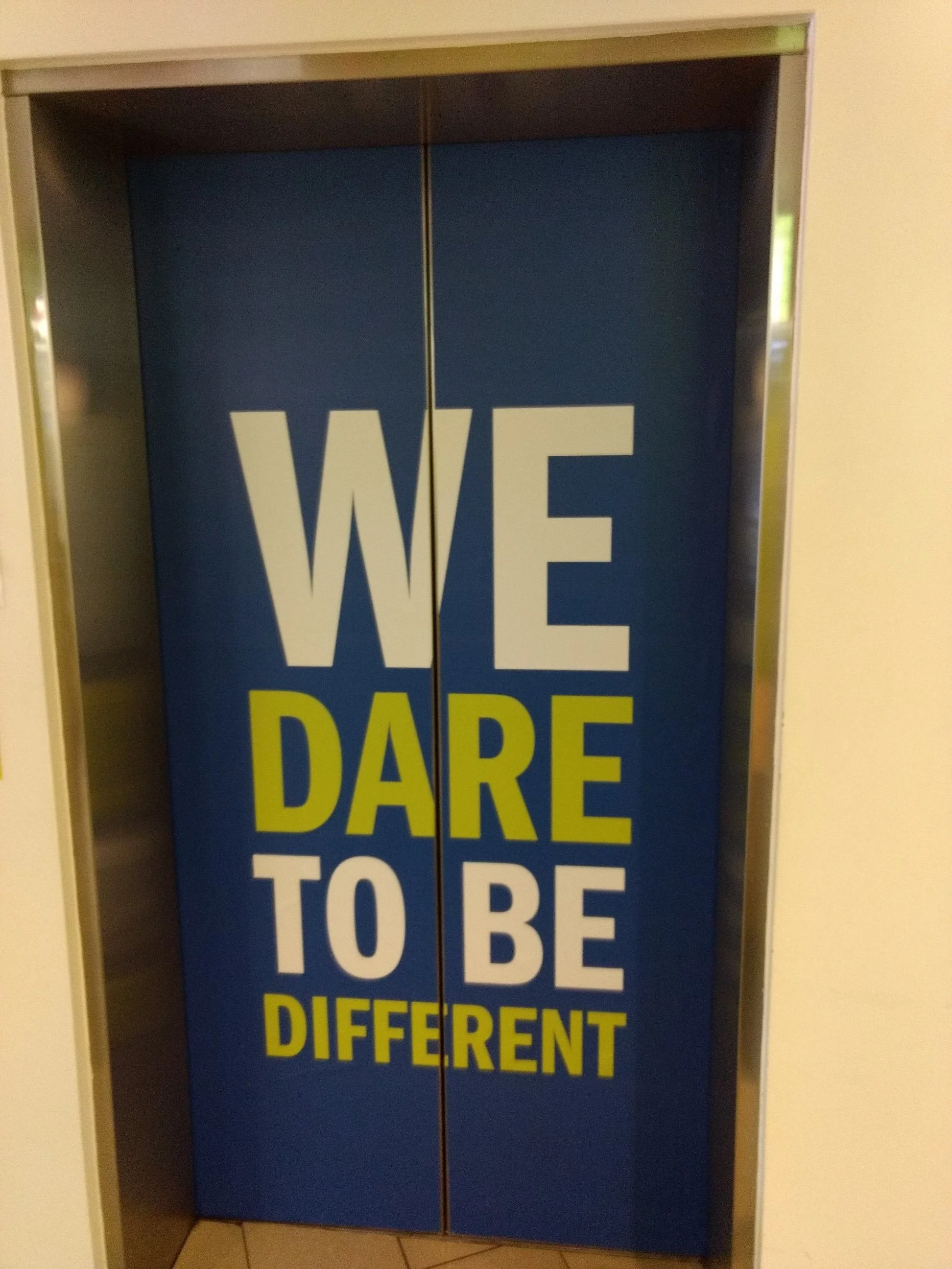 Elevator doors with a sign that reads, 'WE DARE TO BE DIFFERENT' in bold letters.