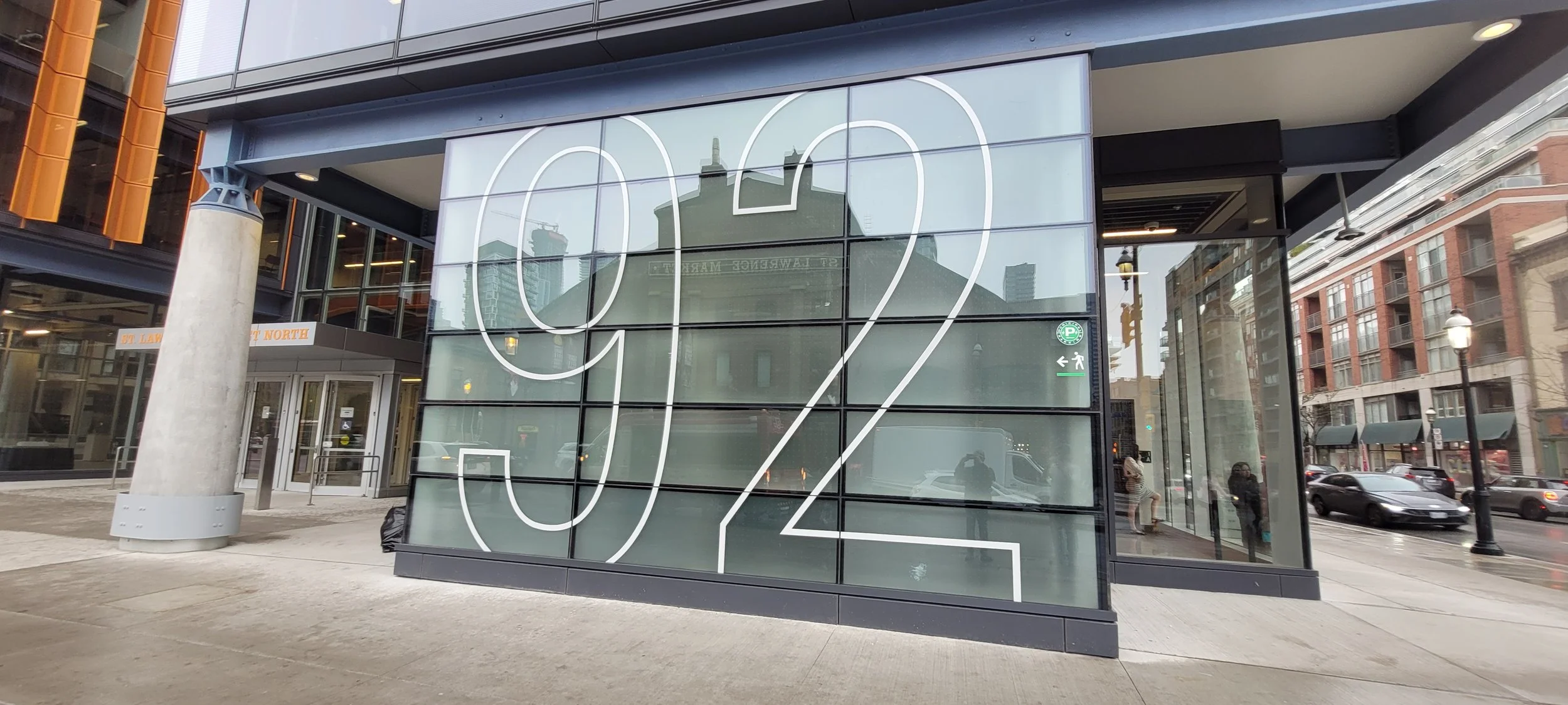 A large glass window with the numbers '92' outlined in white on it, reflecting buildings and street scene outside.