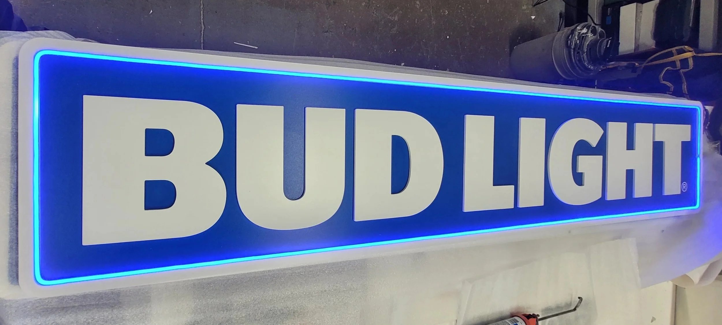 An illuminated blue sign with large white letters reading 'BUD LIGHT' lying on a workbench.