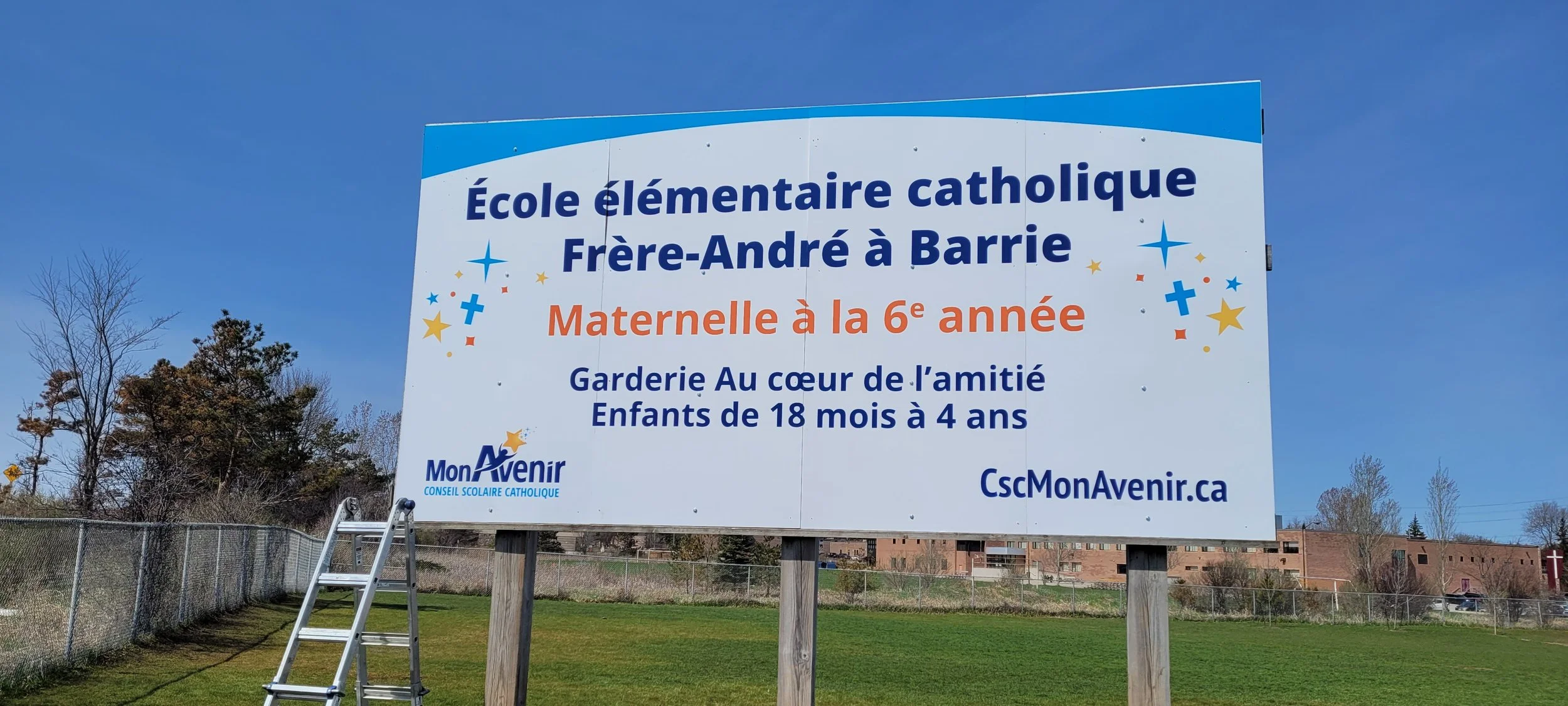 Large outdoor sign for Frère-André Catholic Elementary School in Barrie, indicating it is a kindergarten for 6th grade, with emphasis on friendship and children ages 18 months to 4 years, under the Mon Avenir program.