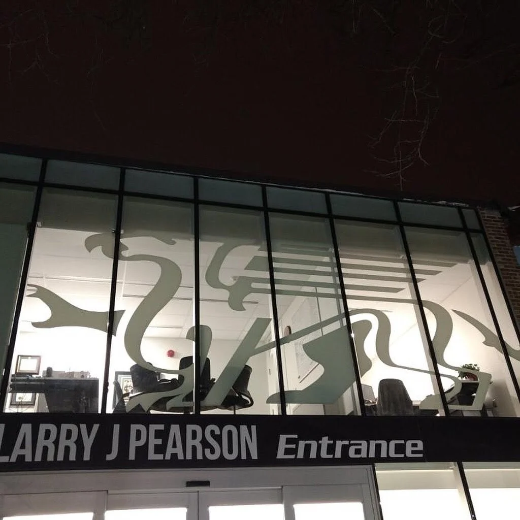 Office building with large glass windows decorated with dragonfly and dragon designs, with a sign reading 'Larry J Pearson Entrance' at the entrance.