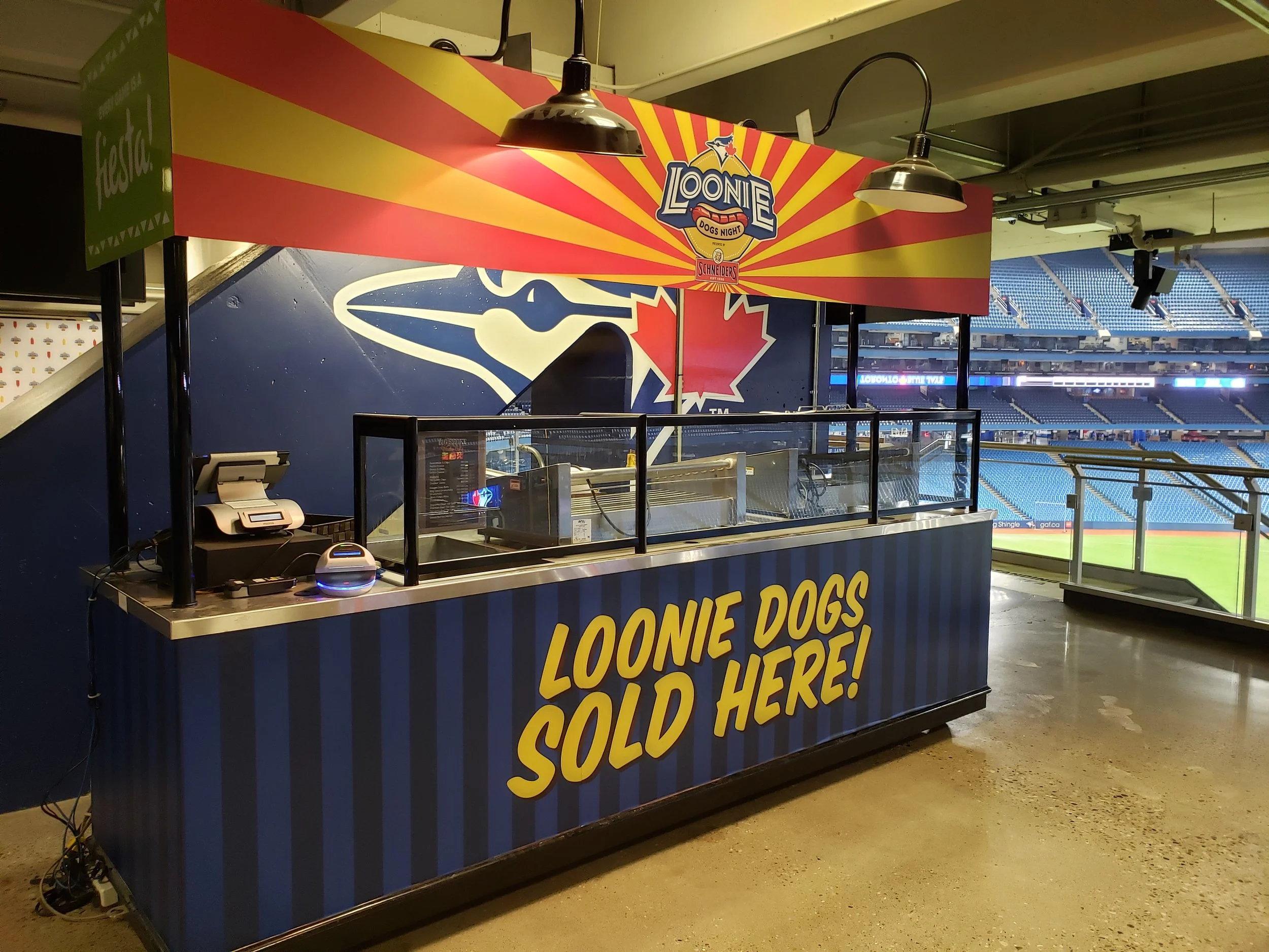 Blue Jays branded Loonie Dogs hot dog stand at a sports stadium with seating visible in the background.